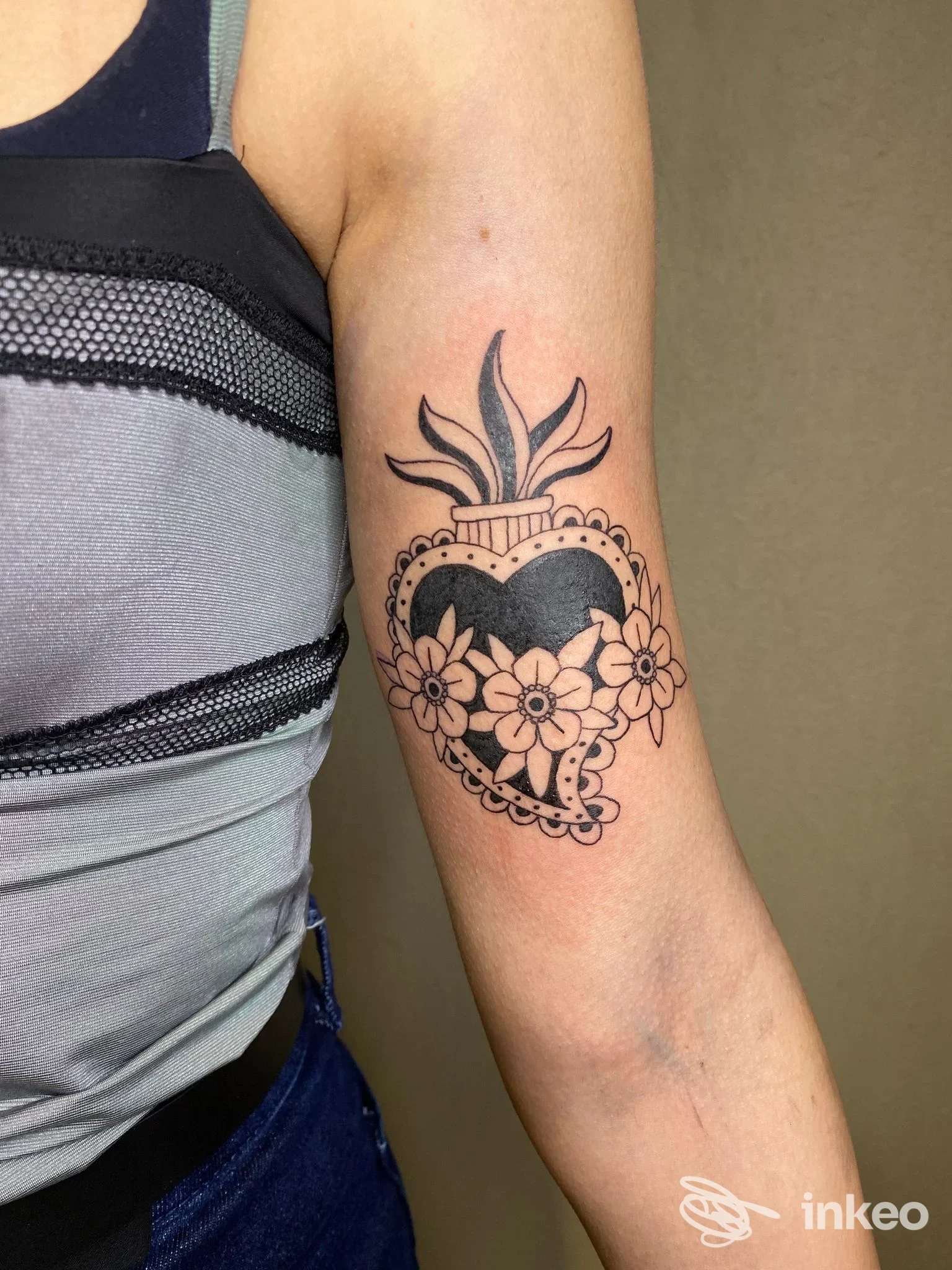 Tatuaggio nero a forma di cuore con fiori sul lato interno del braccio, foto inviata dallo studio Abracadabra di Cagliari.