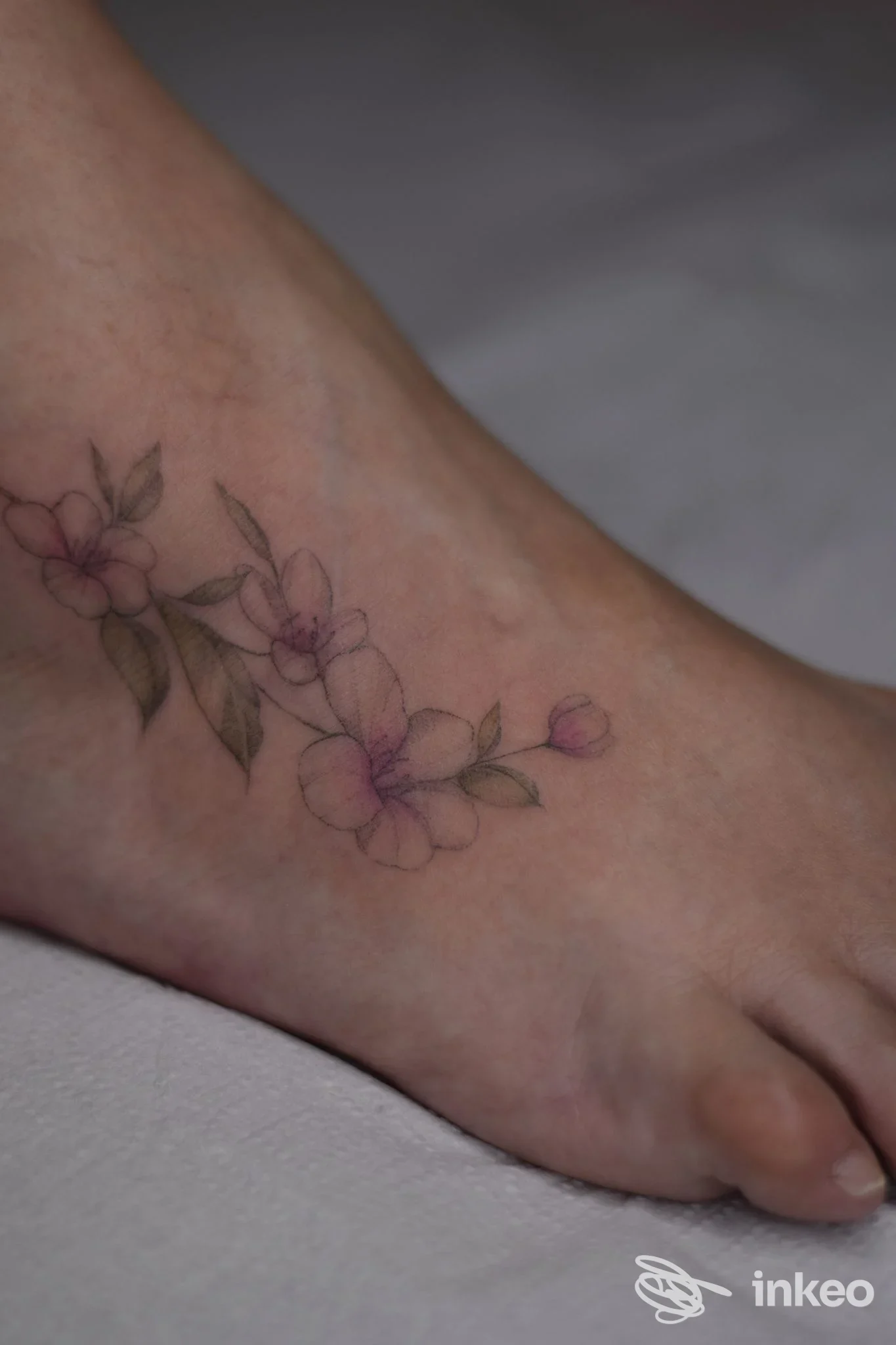 Tattoo floreale delicato sul dorso o lato della caviglia, fiori rosa e foglie su pelle genuina, fotografie non promozionali.