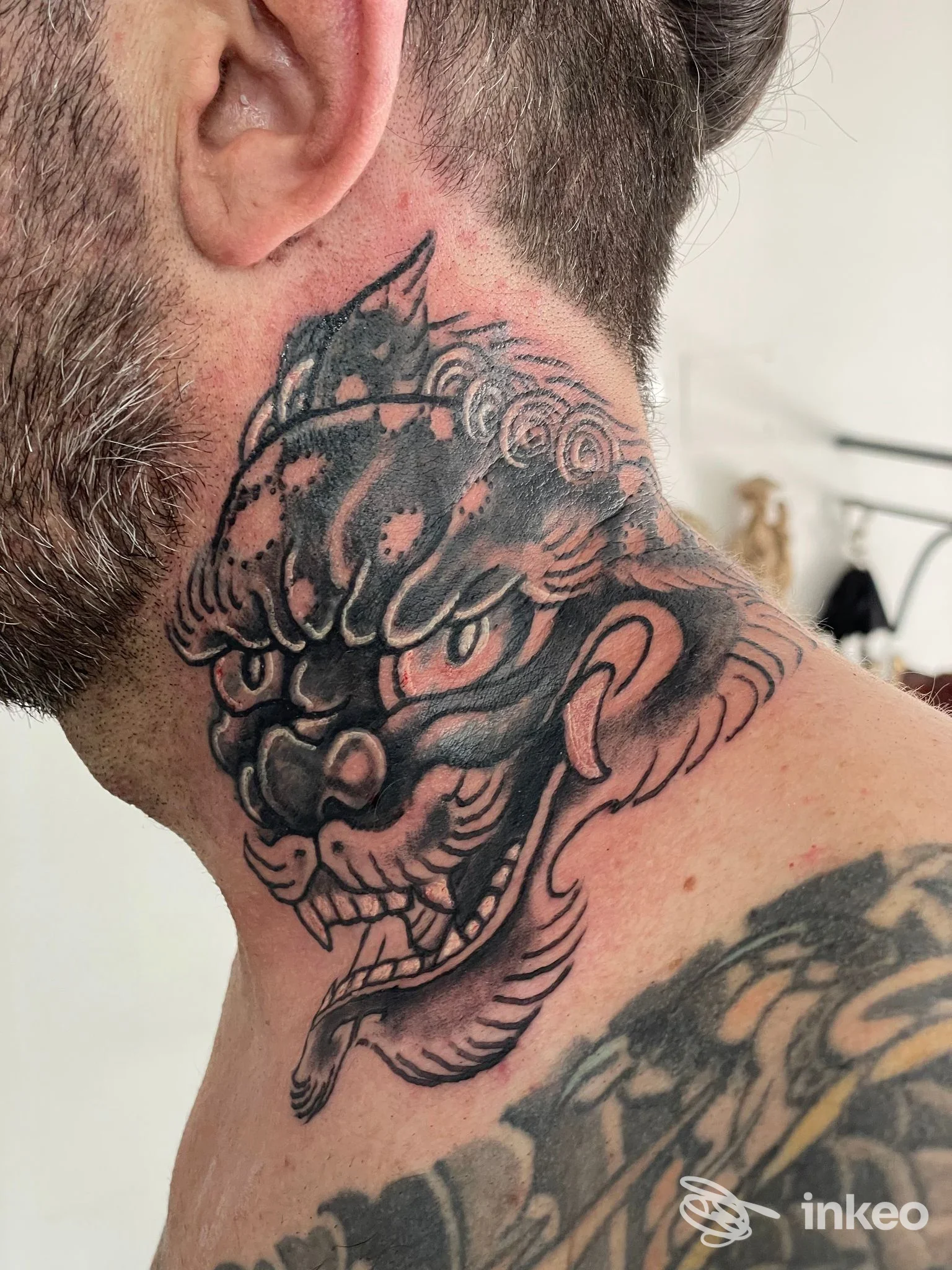 Tatuaggio a maschera in nero e grigio sul lato del collo di un uomo, scatto in primo piano dallo studio Shangri-La, Genova.