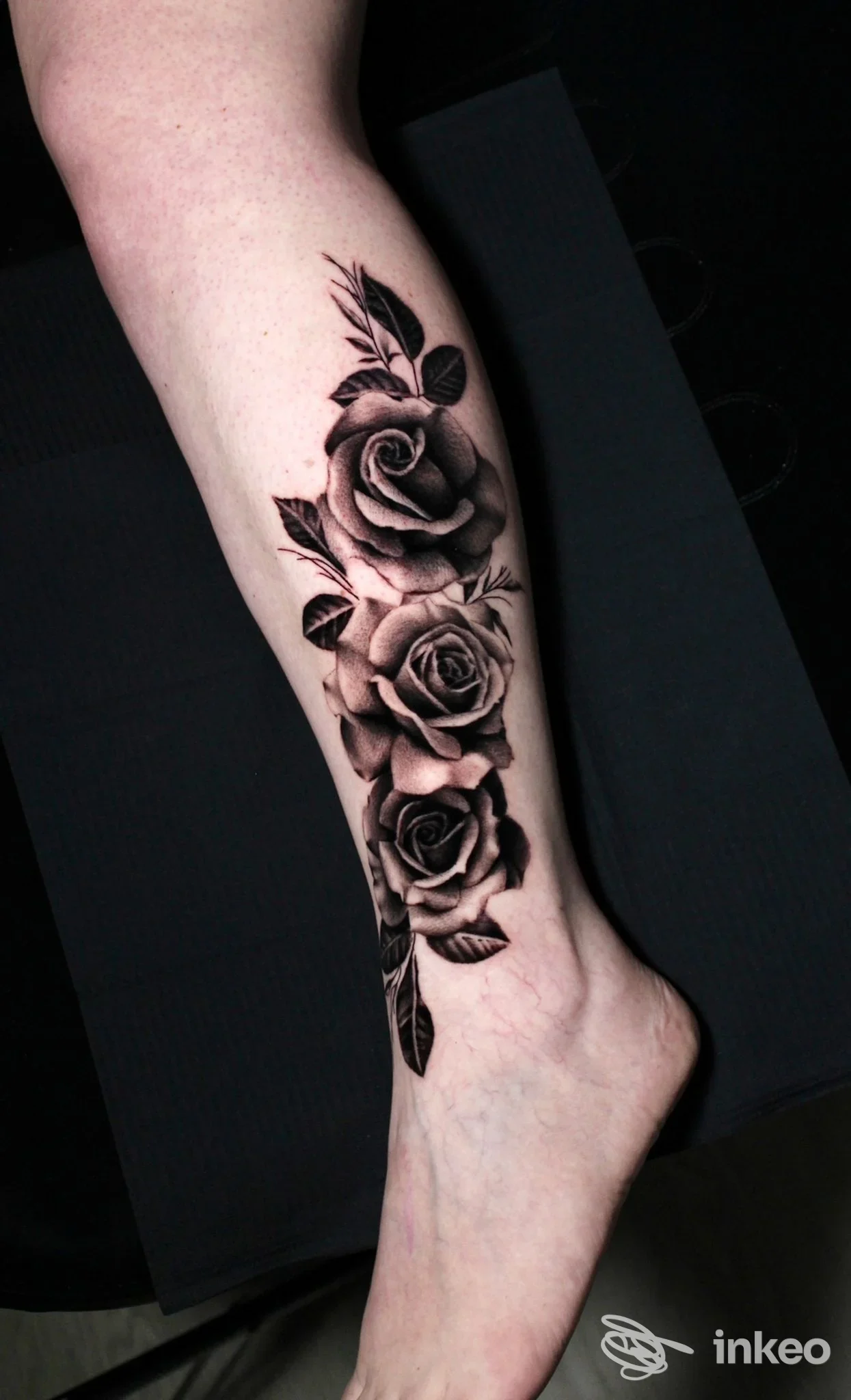 Tatuaggio realistico in bianco e nero di rose che corre lungo la parte anteriore della gamba, lungo tibia, visibile sul piede e sul polpaccio.