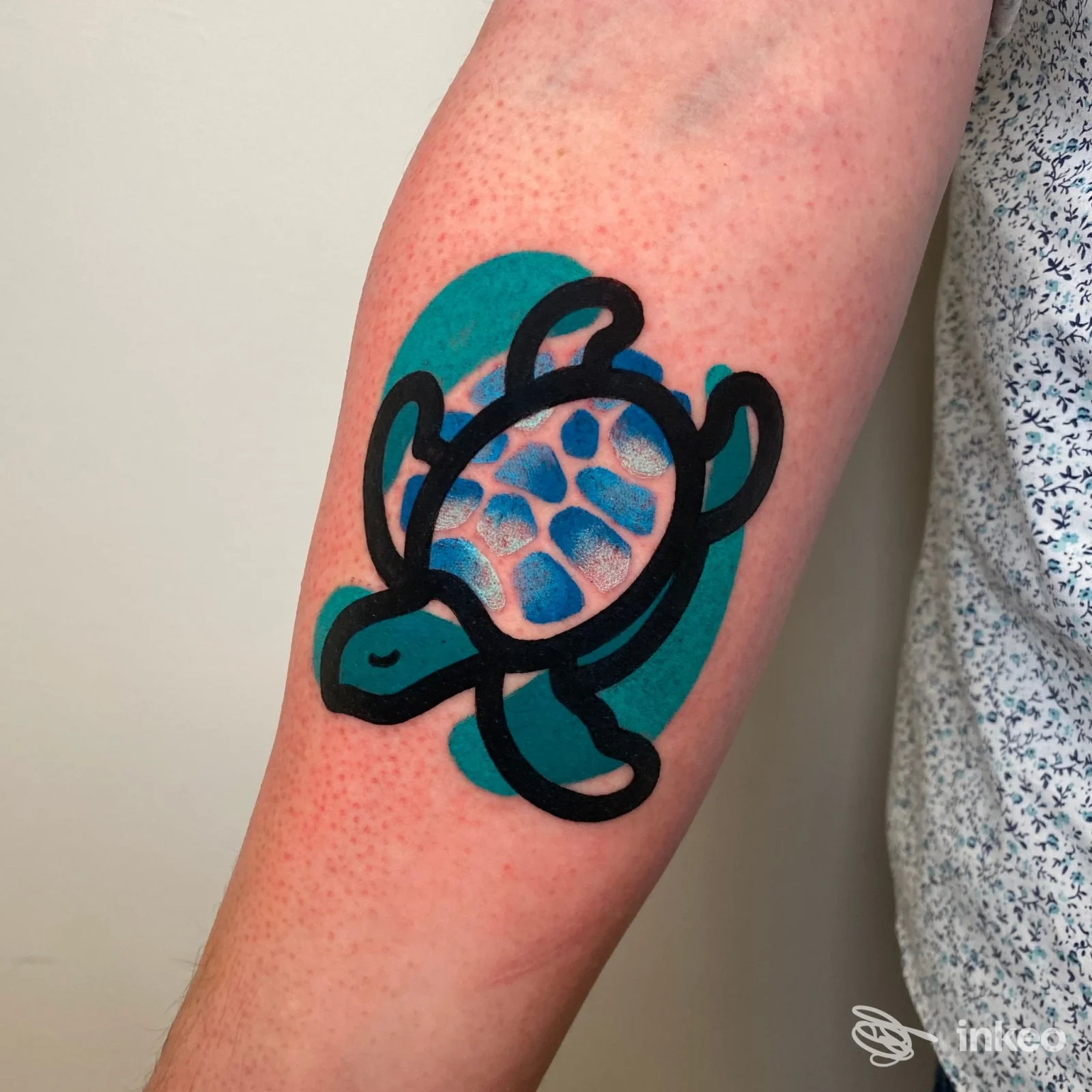 Tatuaggio su braccio raffigurante una tartaruga stilizzata con contorni neri spessi e sfondo verde acqua.
