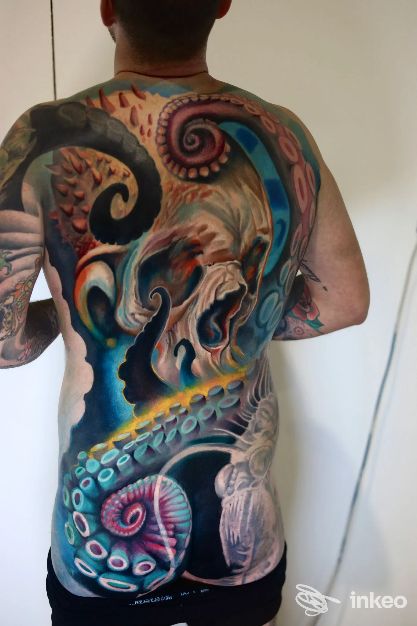 Grande tatuaggio a tutta schiena con polpi e tentacoli nei toni del blu, turchese e rosa, lavoro dettagliato realizzato da Paul White Vision a Barletta.