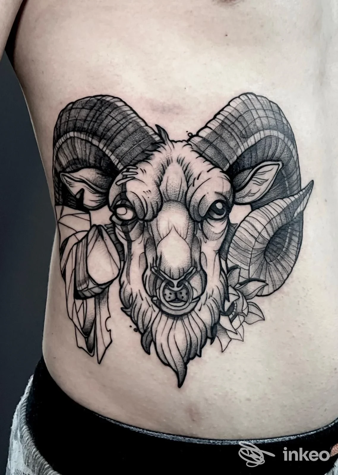 Tatuaggio realistico su pelle visibile: testa di ariete con corna in bianco e nero sul fianco, realizzazione corporea mostrata in primo piano, nessun testo o overlay visivo.