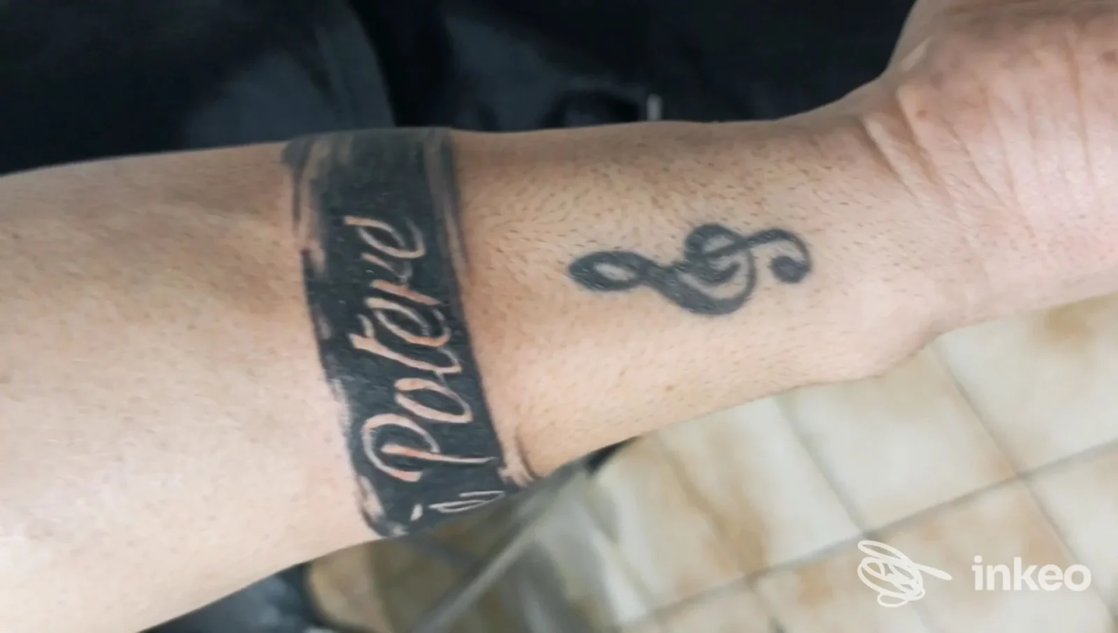 Bracciale tatuato in nero con scritta e piccola chiave di violino su avambraccio; immagine per tattoo e piercing roma, Roma.