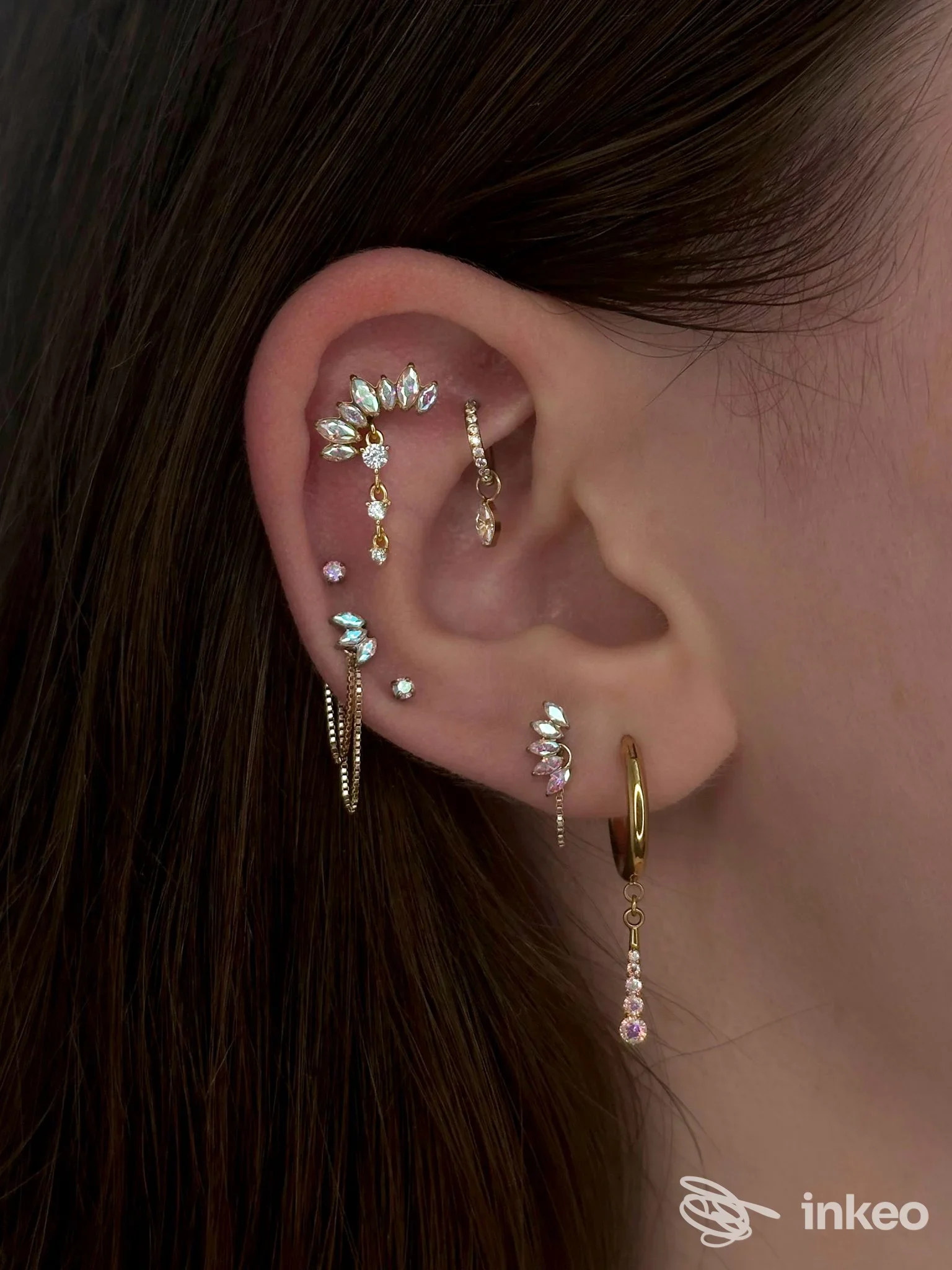 Orecchio sinistro con diverse piercings dorati e zirconi, gioielli pendenti lungo l’orecchio, in primo piano.