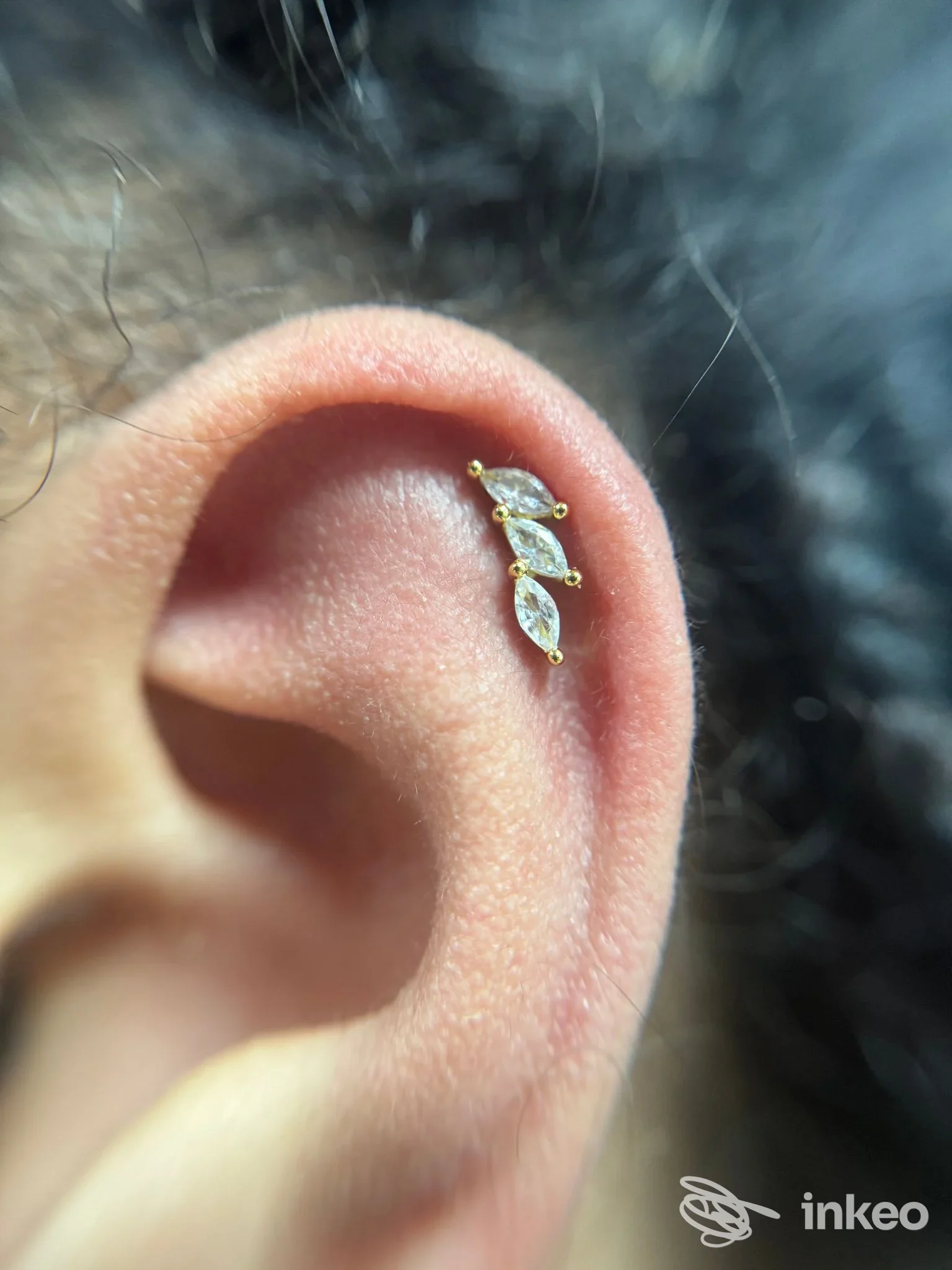 Primo piano di un piercing con tre pietre sull'orecchio; immagine fornita da Derma Room Nuoro, Nuoro.