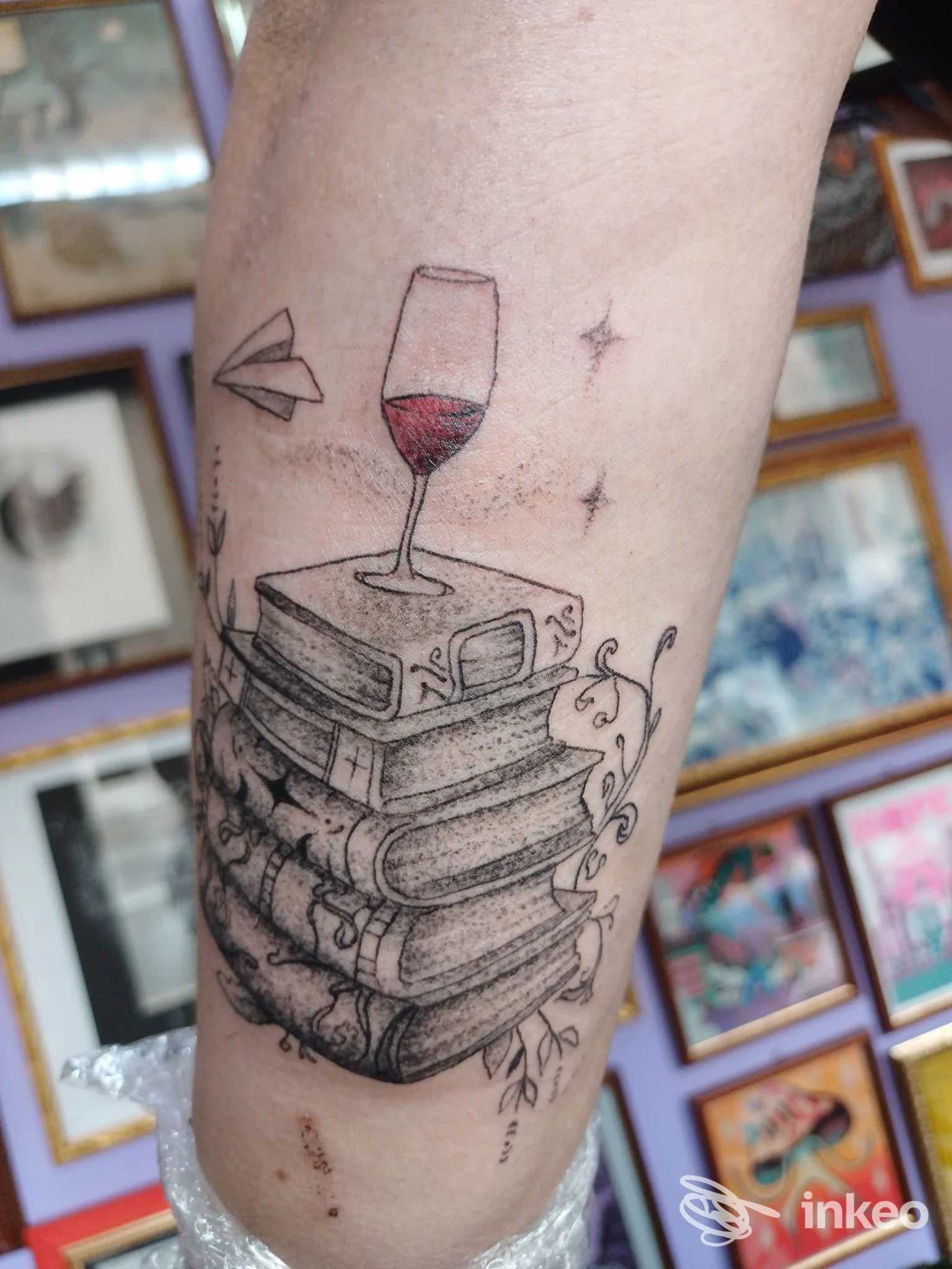 Tattoo sull'avambraccio raffigurante una pila di libri con un calice di vino rosso in cima, decorazioni floreali, eseguito da Coral Inkwell Tattoo.
