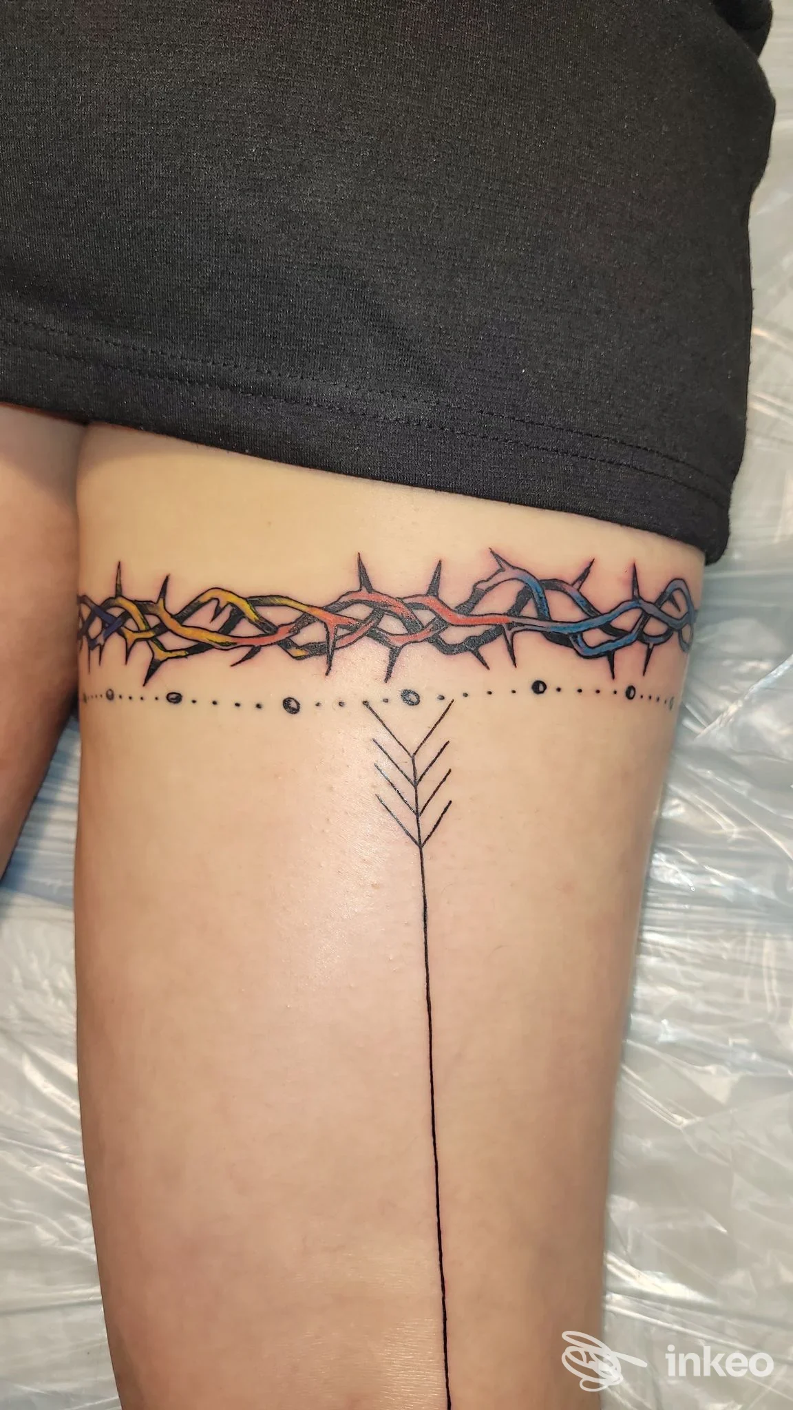 Tatuaggi sulla coscia: fascia di filo spinato colorato e linea verticale con freccia, Artè Tattoo, Bisceglie.