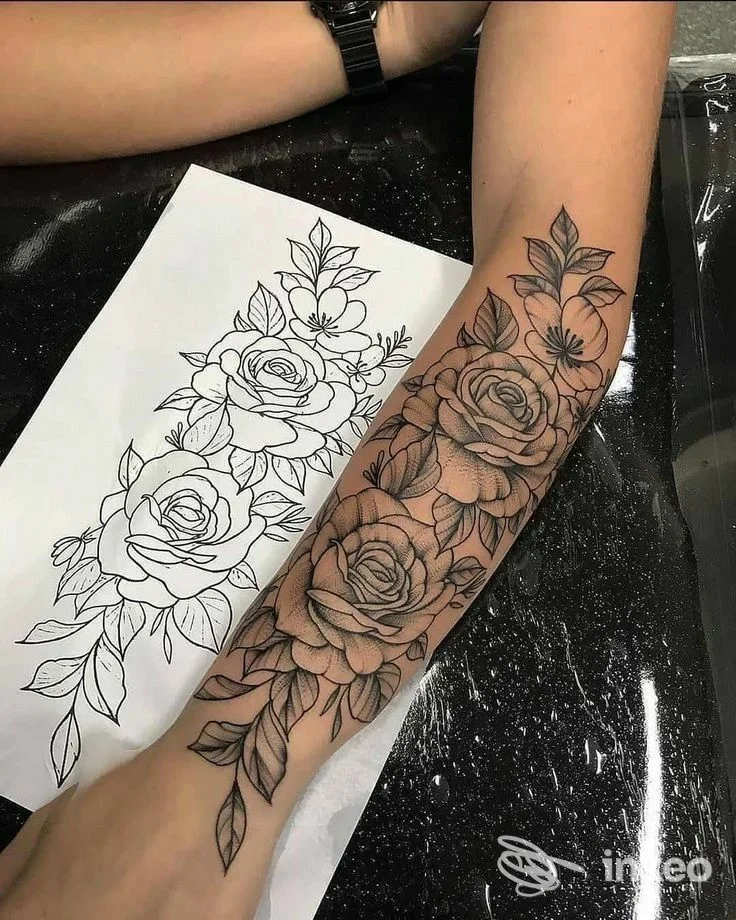 Ampio tatuaggio floreale nero/grigio sull'avambraccio, fotografato accanto al disegno cartaceo. Immagine di TATTOO FLOWER, Seregno.