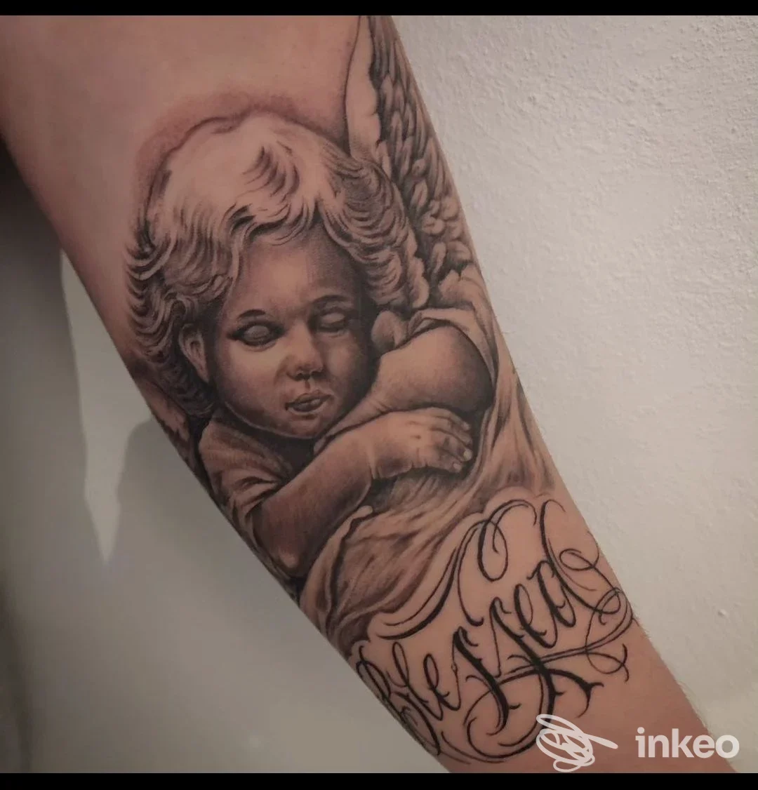 Primo piano di un tatuaggio realistico sull'avambraccio con un angelo cherubino e lettering ornamentale. Mino ink Tattoo Store, Mugnano di Napoli.