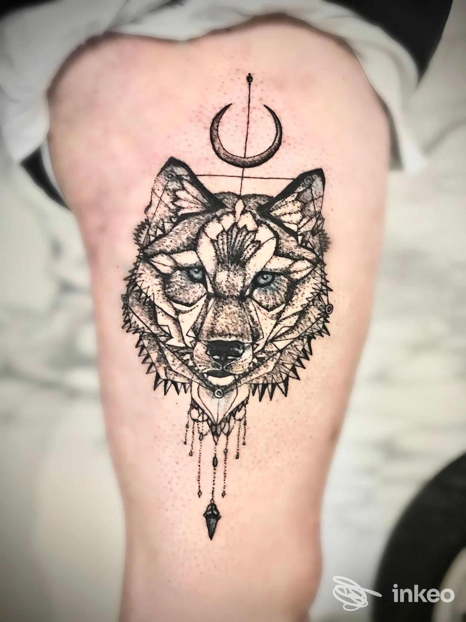 Tatuaggio a inchiostro nero di un lupo geometrico con mezzaluna e pendenti sulla coscia, fotografato da Endo Tattoo a Bari.
