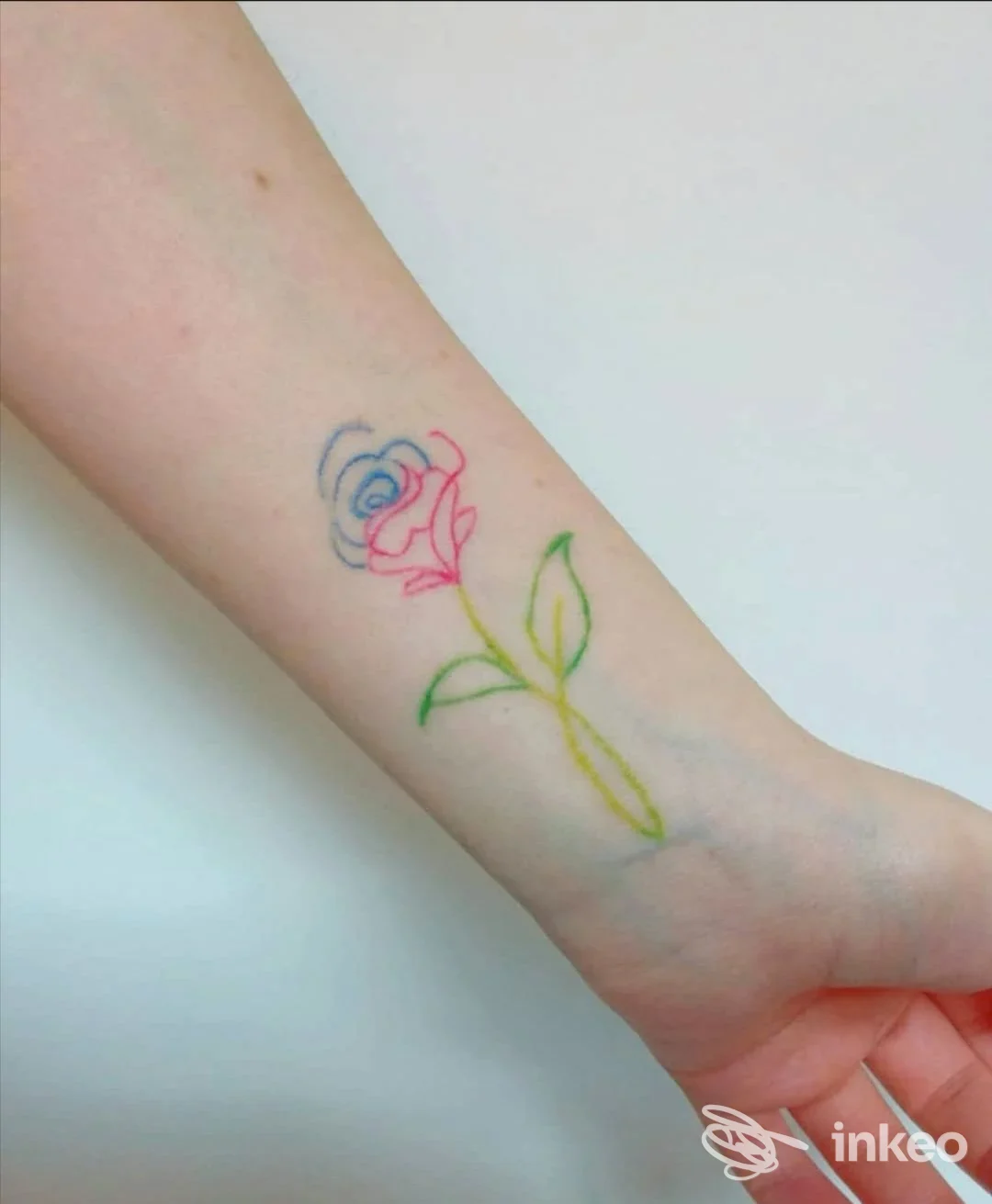 Primo piano di un tatuaggio a linee sottili raffigurante una rosa multicolore sull'avambraccio interno. Art Studio Tattoo di Angela Magagnoli, Cento.