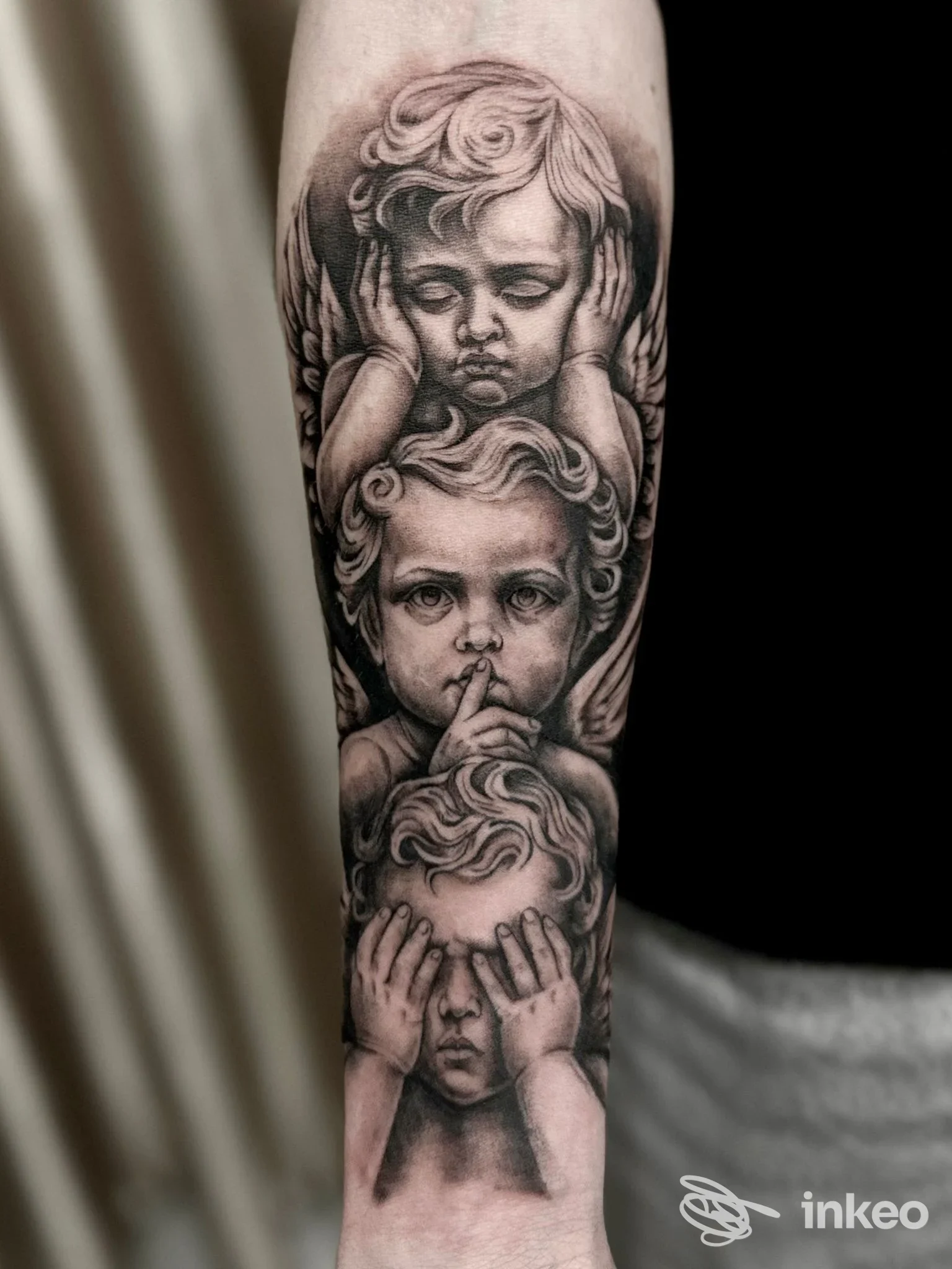 Tatuaggio realistico in bianco e nero di tre angeli cherubini sull'avambraccio, realizzato da Just Think Tattoo a Chieti.