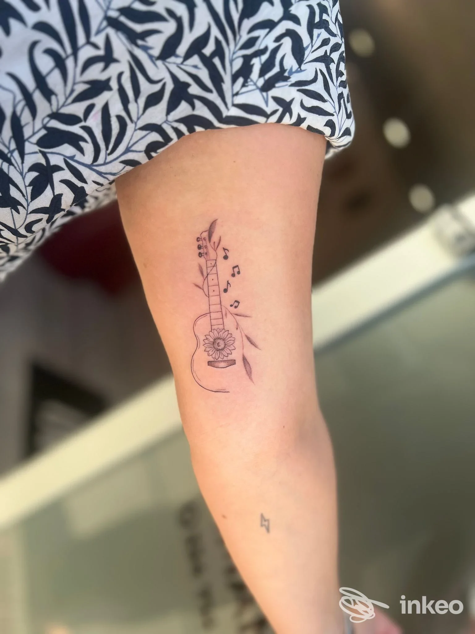 Tatuaggio fineline a forma di chitarra con note e foglie sul braccio interno, MEMM INK, Venosa.