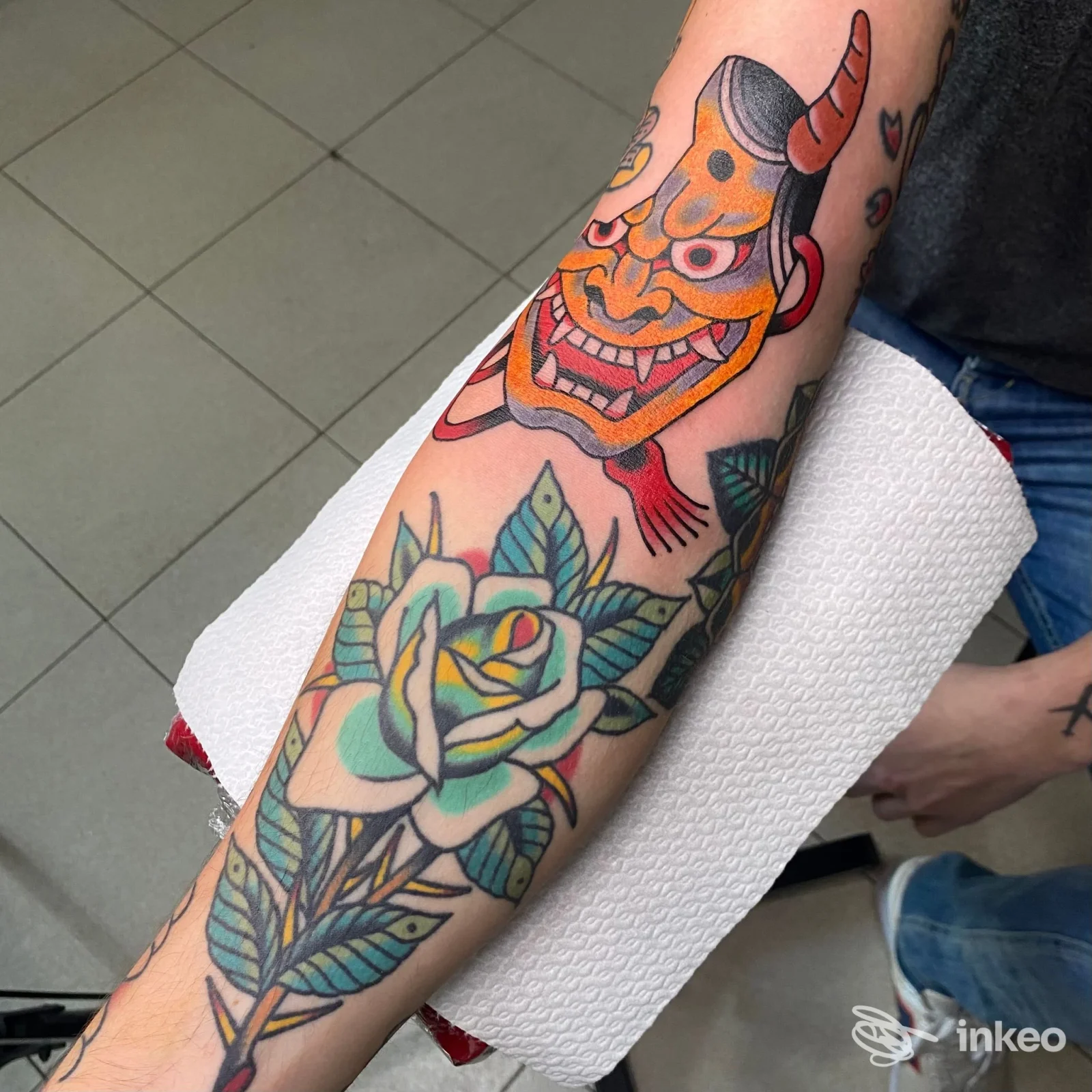 Tatuaggi colorati su avambraccio: maschera tradizionale e rosa stilizzata, foto dallo studio The other skin tattoo a Fiano Romano.