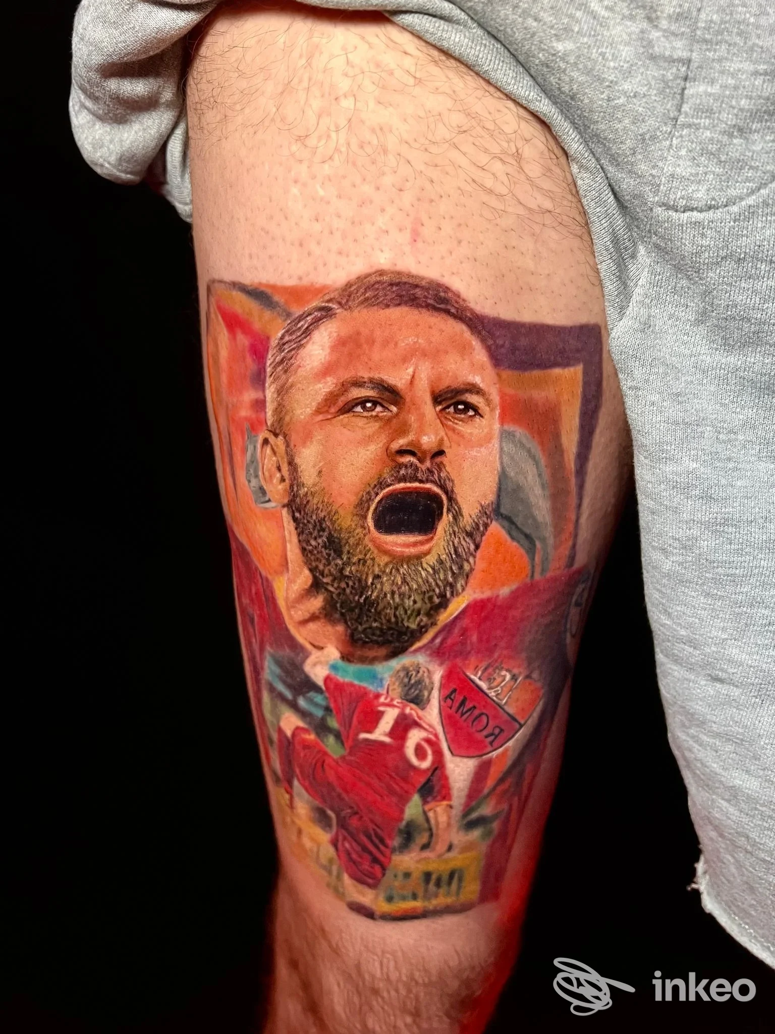 Tatuaggio realistico su coscia realizzato da Dark Moon Tattoo, Roma: ritratto a colori e scena calcistica integrata sul polpaccio.