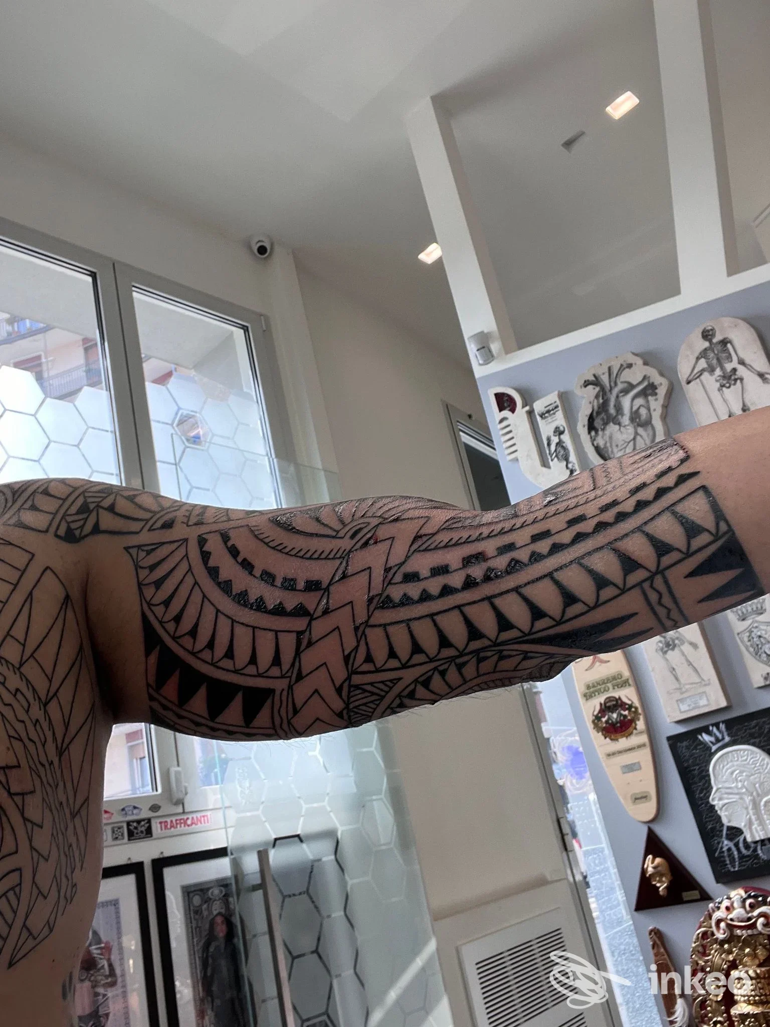 Tattoo geometrico su braccio: parte superiore dell’arto visibile in primo piano all’interno di uno studio, senza viso mostrato.