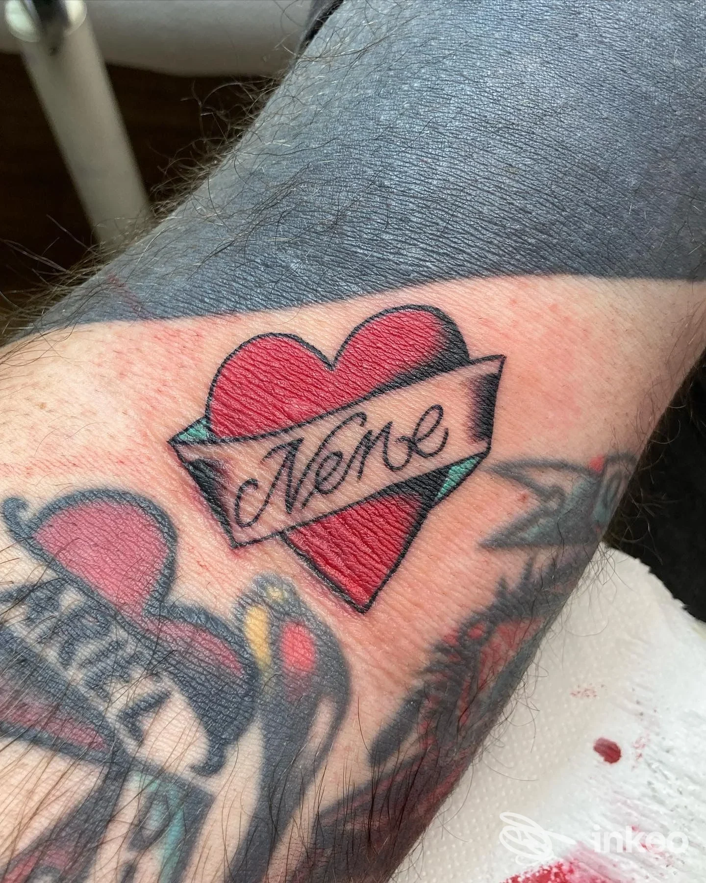 Tatuaggio su avambraccio: cuore rosso con aquila e nastro con scritta, scatto ravvicinato senza volto
