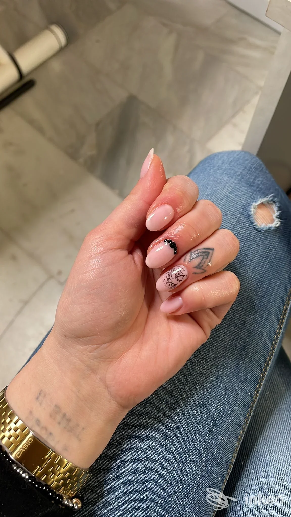 Primo piano di mano e polso con piccoli tatuaggi neri e manicure rosa, foto per Dietro le Quinte di Arianna Pulsoni, Avezzano.