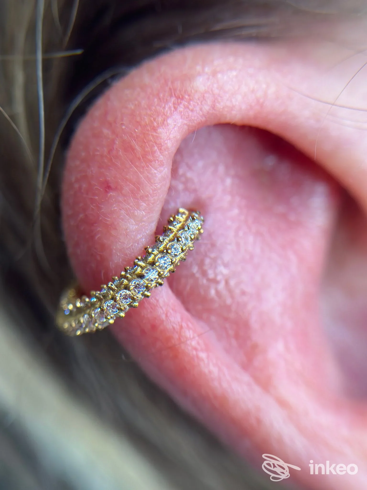 Primo piano di un piercing a cerchio dorato con pietre sull'orecchio, immagine per ChiaraG Beauty expert a Lipomo.