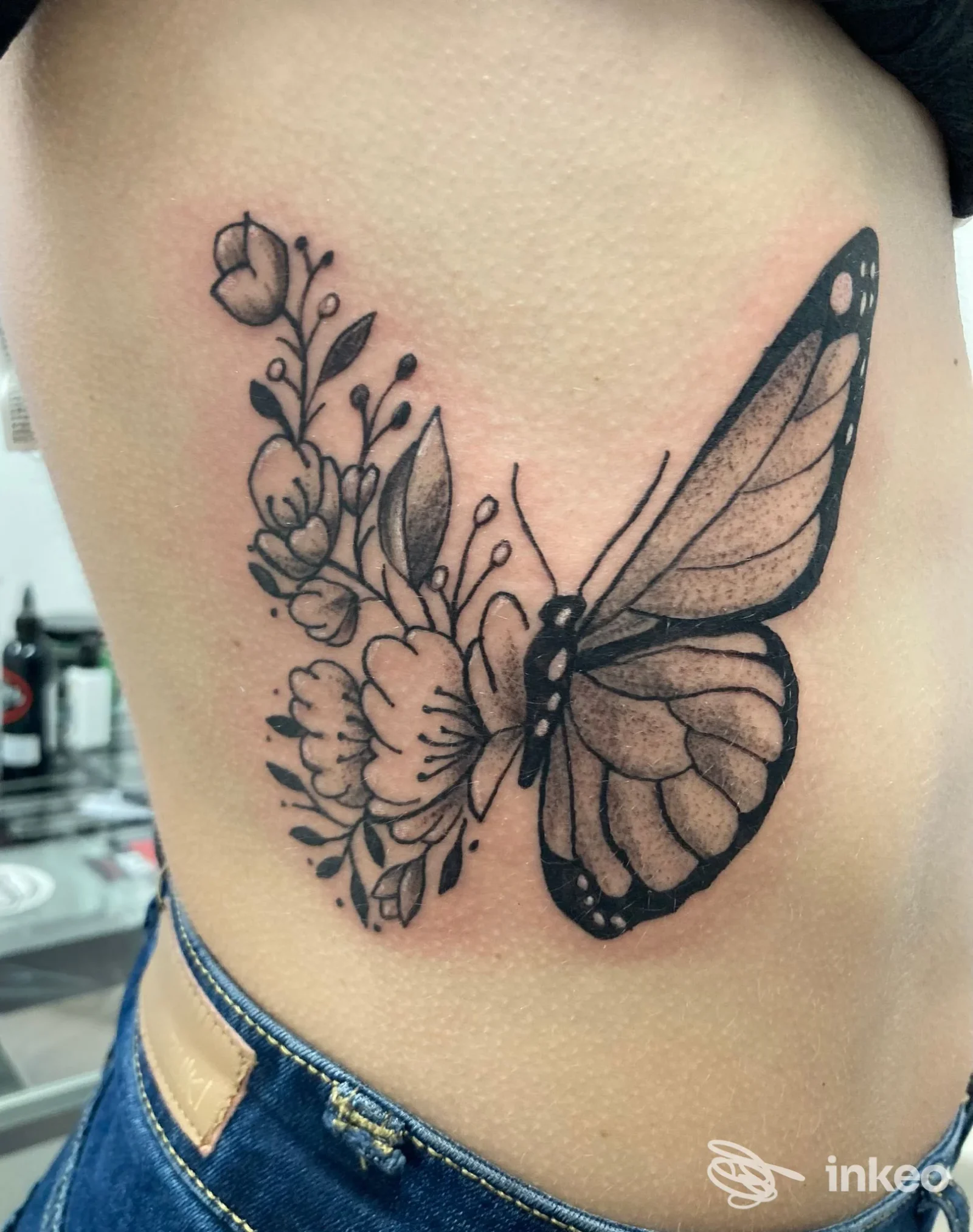 Tattoo floreale con grande farfalla nera e sfumature grigie lungo il fianco, eseguita sulla pelle. Nessun volto visibile nell’immagine.