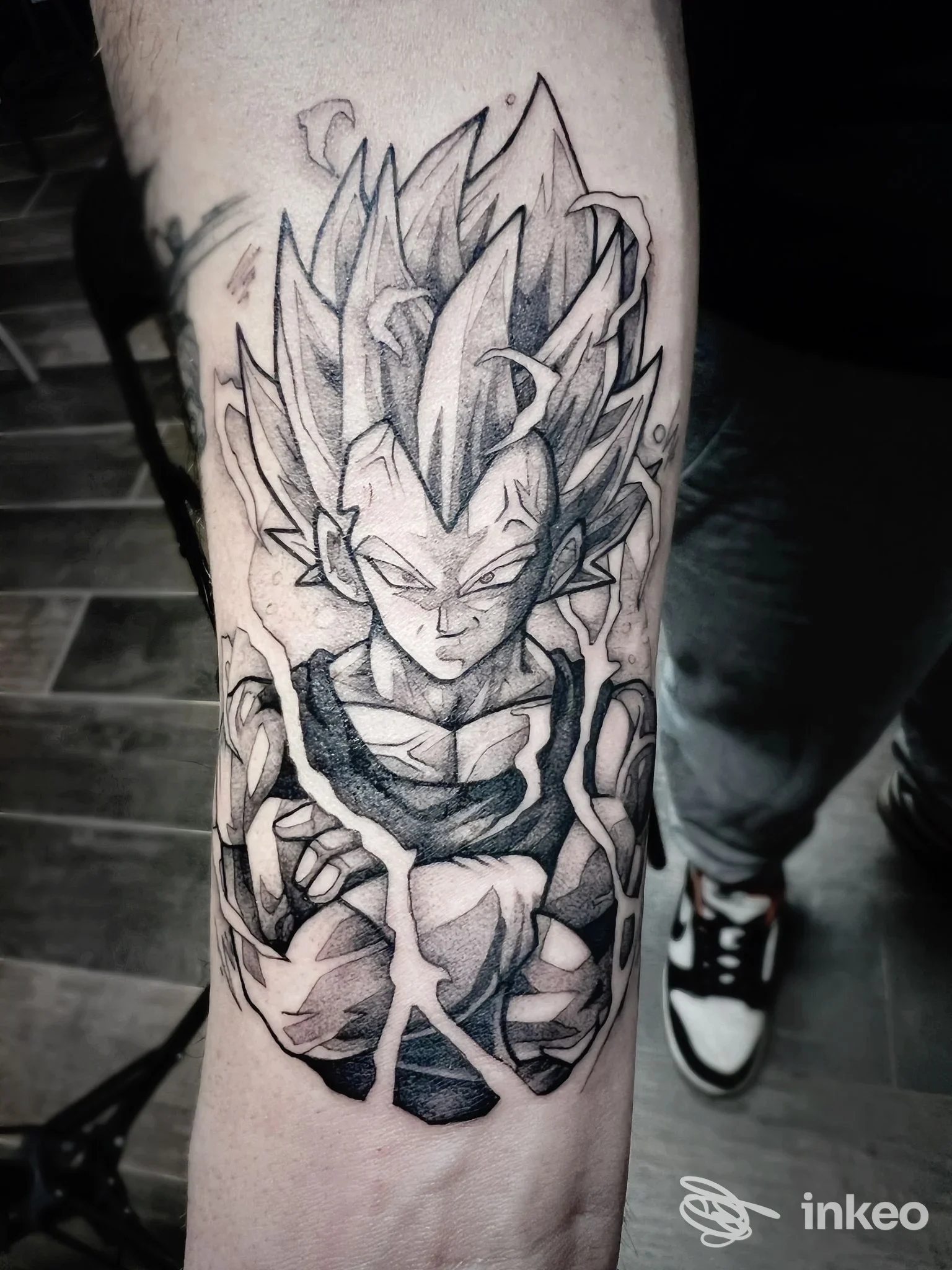 Tattoo inchiostrato in bianco e nero su gamba, figura stilizzata di Super Saiyan con capelli appuntiti e dettagli muscolari, esecuzione nitida e contrasti marcati.