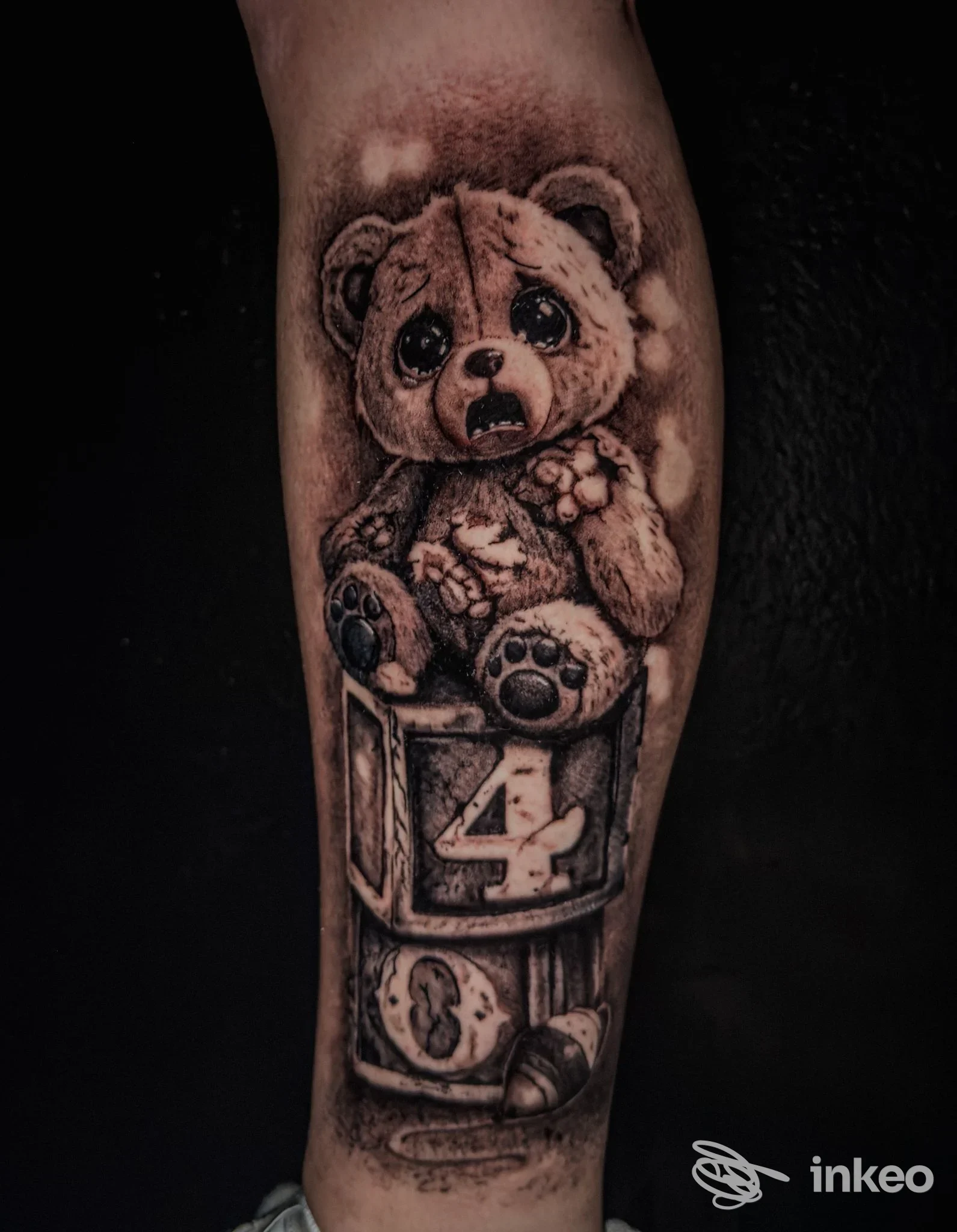 Tatuaggio realistico in bianco e nero di un orsacchiotto su blocchi numerati sull'avambraccio. Beauty & the Beast Tattoo Studio, Mondovì.