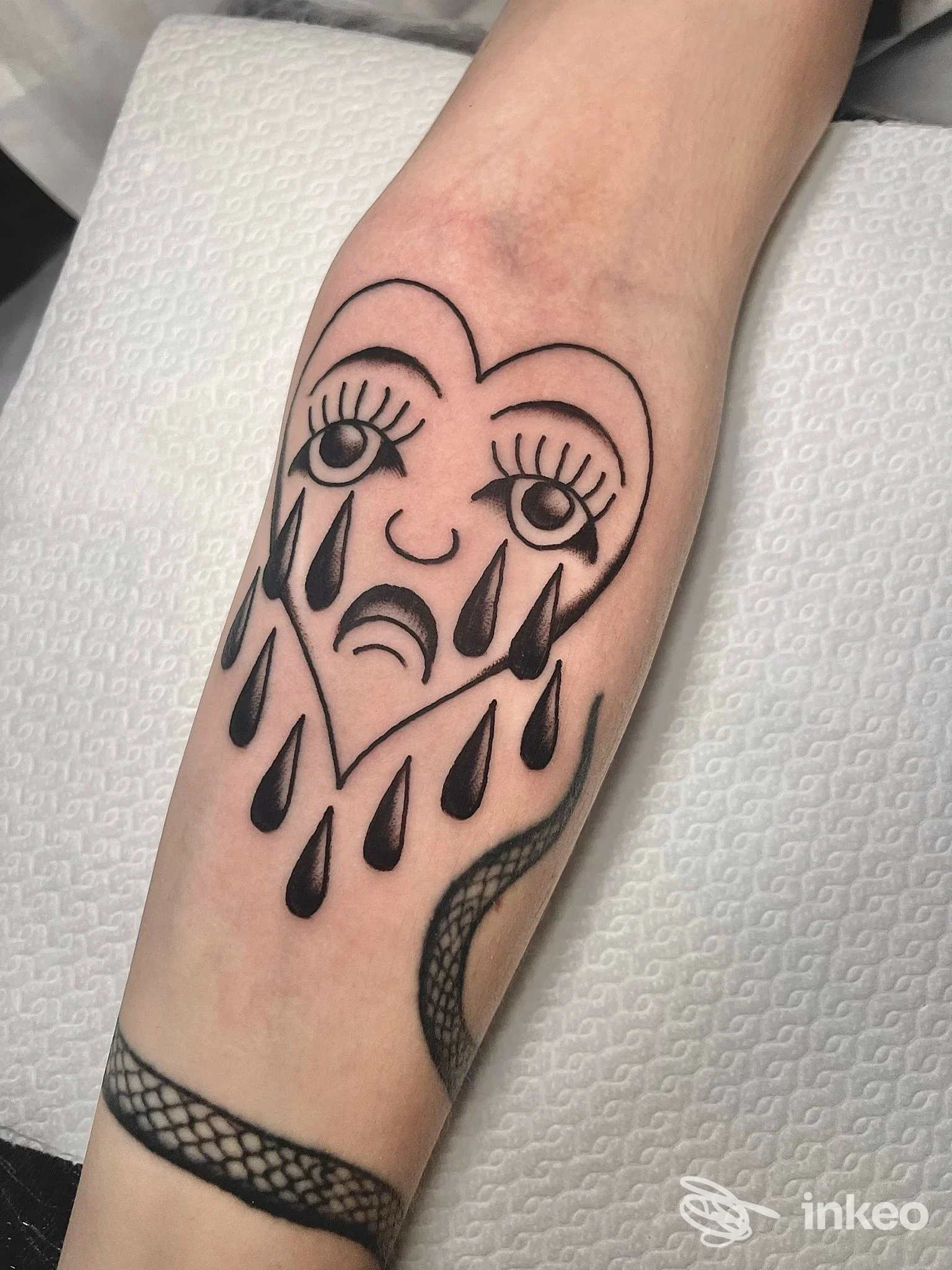 Tatuaggio a linee nere di un cuore piangente e serpente sull'avambraccio, Bassetti Tattoo e Piercing, Roma.