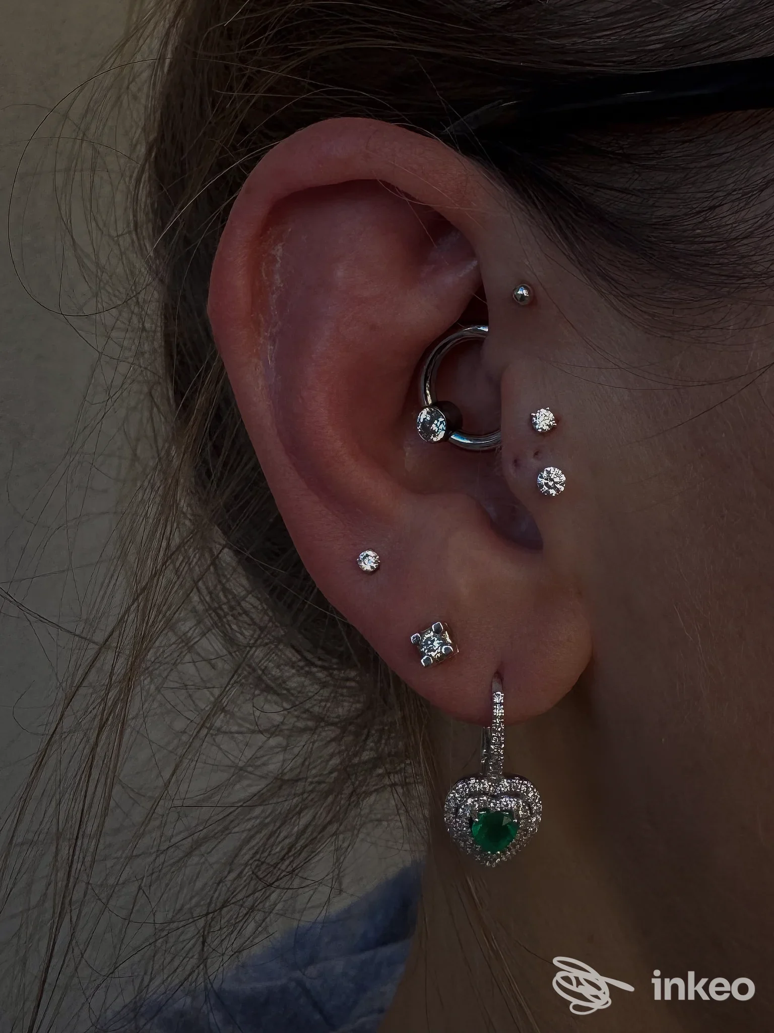 Primo piano di orecchio con multipli piercing e pendente a cuore verde, foto inviata da Borneoflower Piercing Studio, Sanremo.