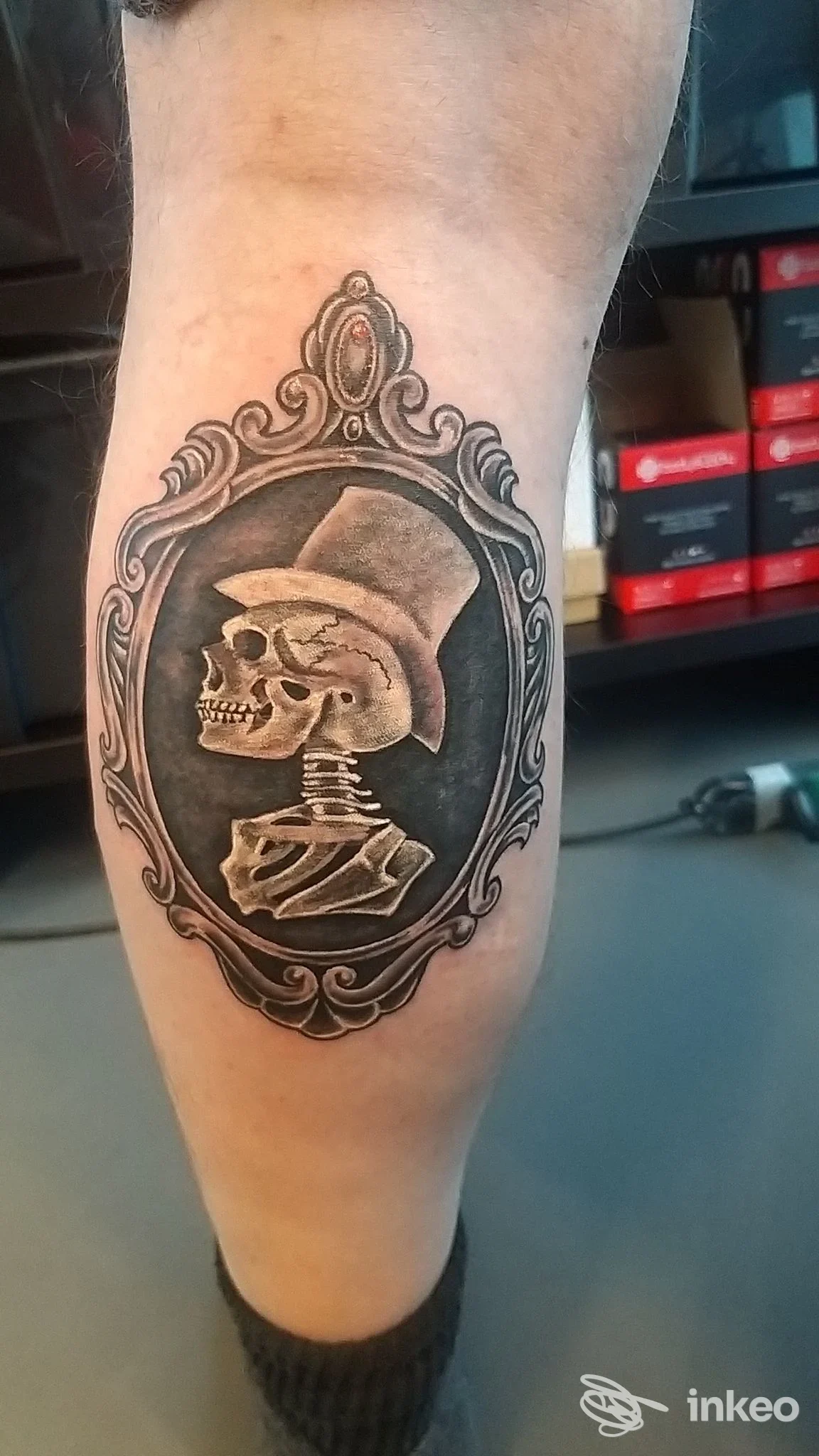 Tatuaggio sul polpaccio: teschio con cilindro dentro una cornice ornamentale, realizzato da Sacrum Cor a Zanè.