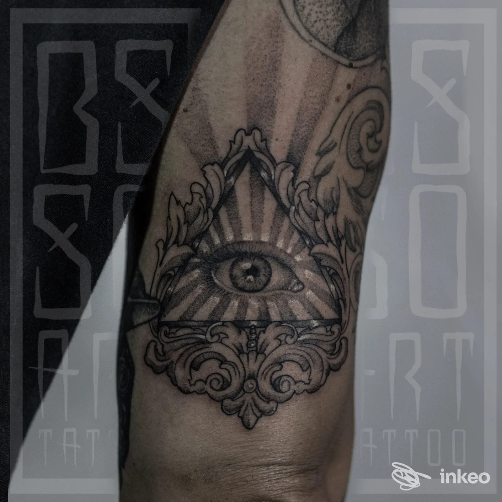 Tattoo sull'avambraccio sinistro: occhio all'interno di un triangolo con raggi e motivi decorativi, visibile senza volto.