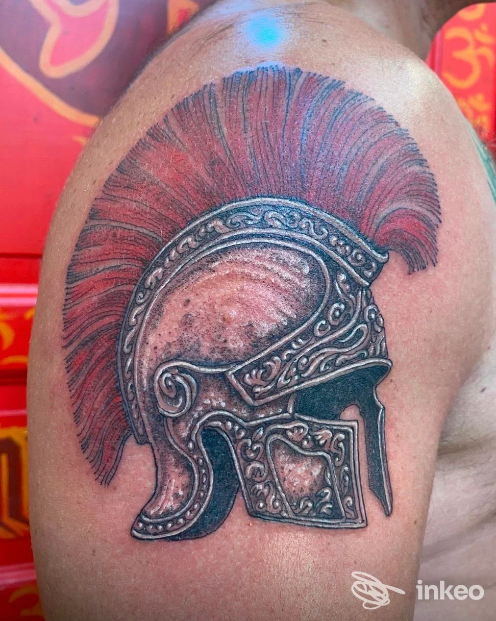 Tatuaggio su spalla raffigurante un elmo romano con cresta rossa, lavoro su pelle fotografato per The Grim Reaper Tattoo, Roma.