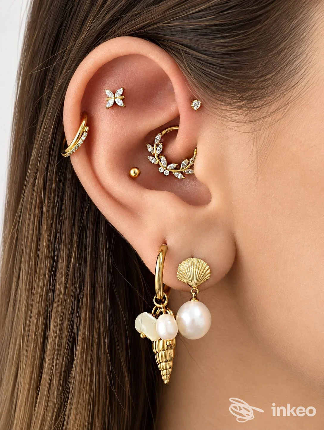 Primo piano di orecchio con più piercing in oro e perle, scatto promozionale di Louis Studio a Torino.