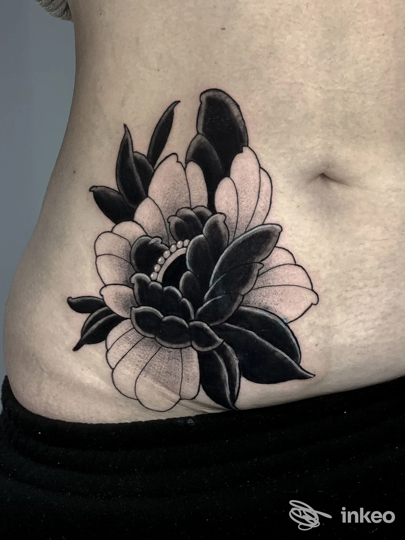 Grande fiore tatuato in nero e ombreggiature sul fianco/addome. Immagine fornita da Skin Beauty Estetica e Tattoo by abbronzatissimi, Senigallia.