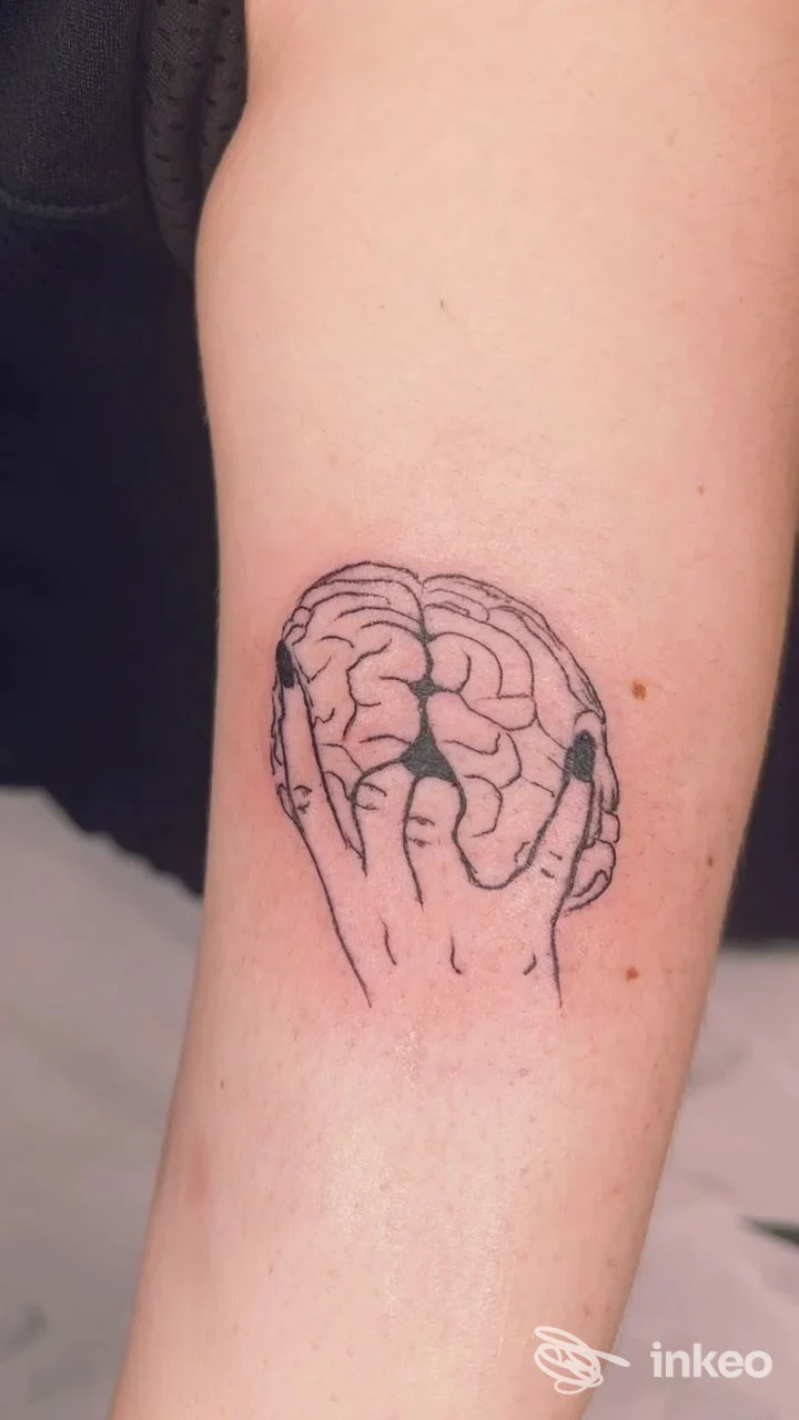 Tatuaggio lineare nero di un cervello tenuto da mani sull'avambraccio, scatto dello studio CHLOE' TATTOO ESTETICA a Jesi.