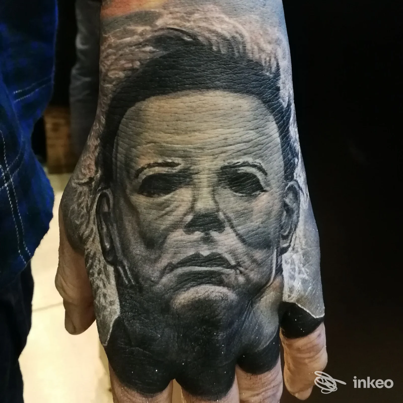 Tatuaggio realistico in bianco e nero sul dorso della mano, ritratto mascherato eseguito da Tattoo Experience ad Ancona.