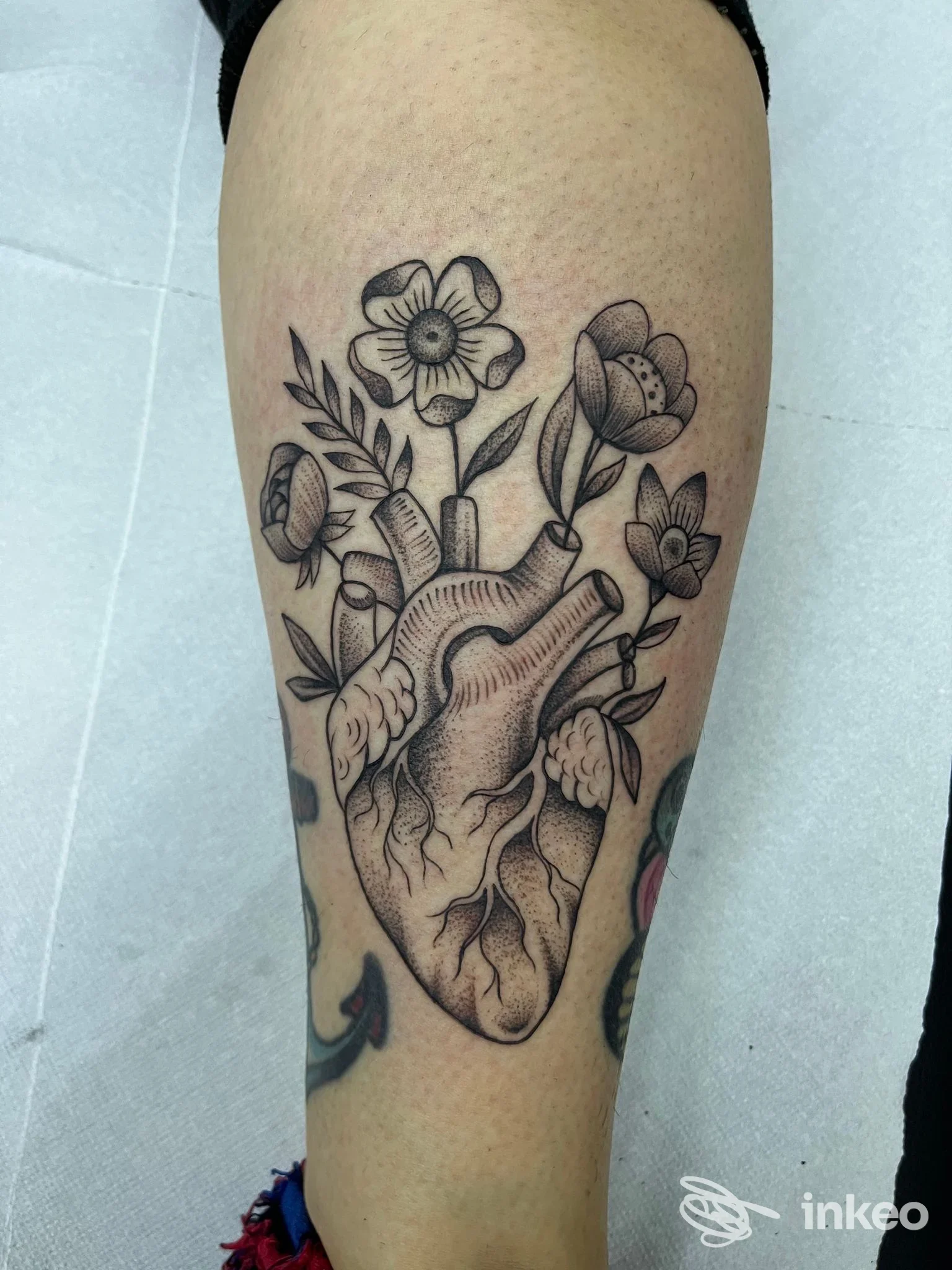 Tatuaggio su polpaccio raffigurante un cuore anatomico da cui sbocciano fiori — Angela Smisek, Termoli.