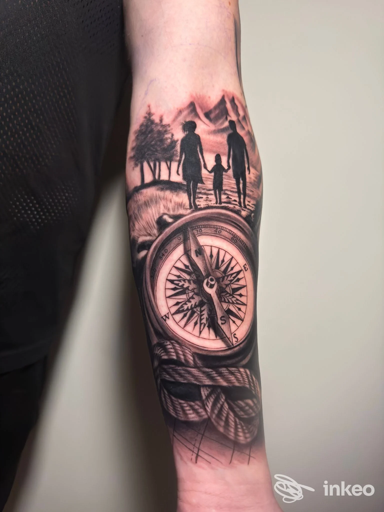 Tatuaggio realistico in bianco e nero sull'avambraccio con bussola e silhouette familiare, realizzato da STORIE DI VITA SU PELLE, Fossano.