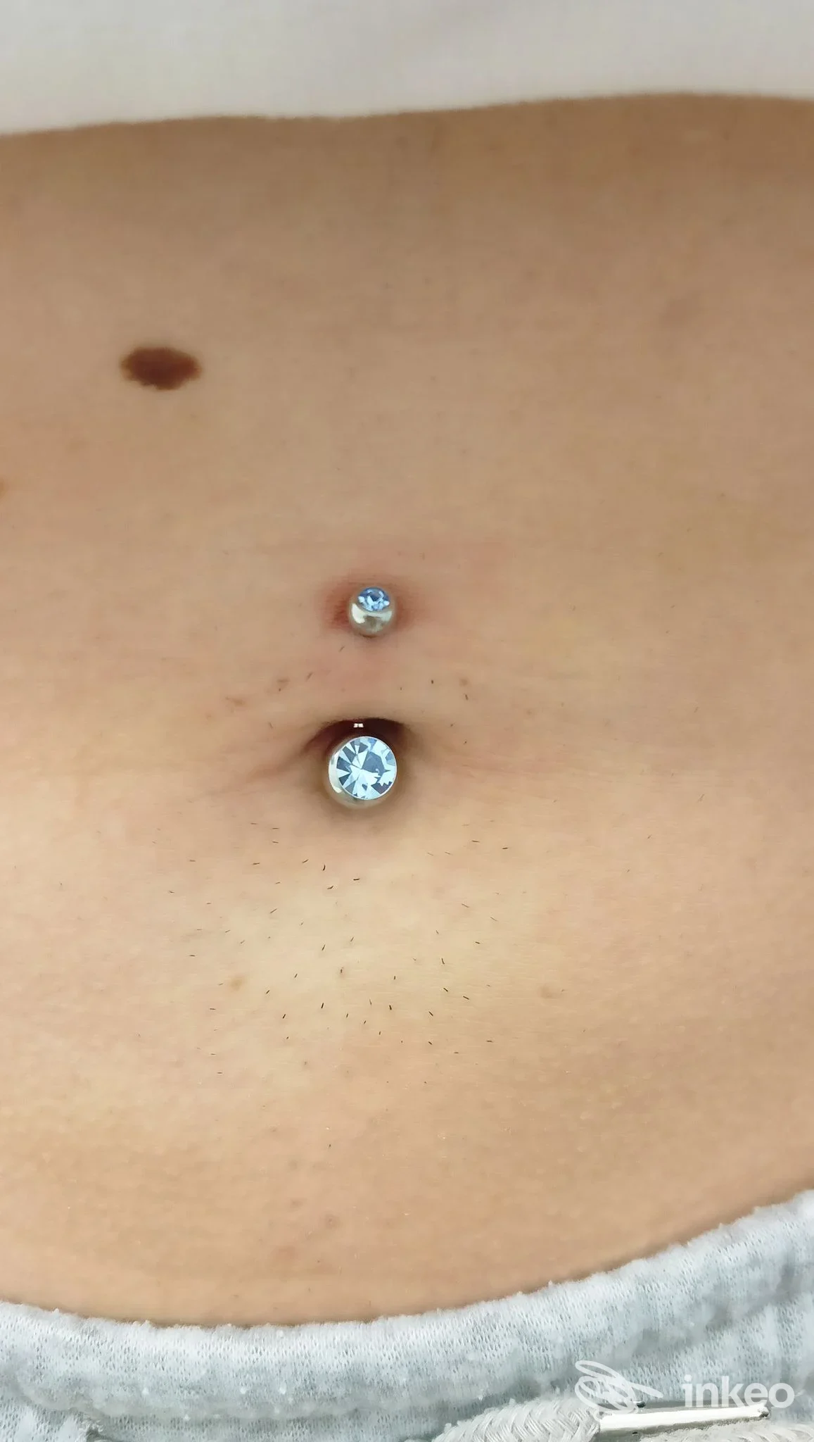 Primo piano di un piercing all'ombelico eseguito da Crazy di Sabrina Graglia a Cigliano, con due gemme visibili sulla pelle.