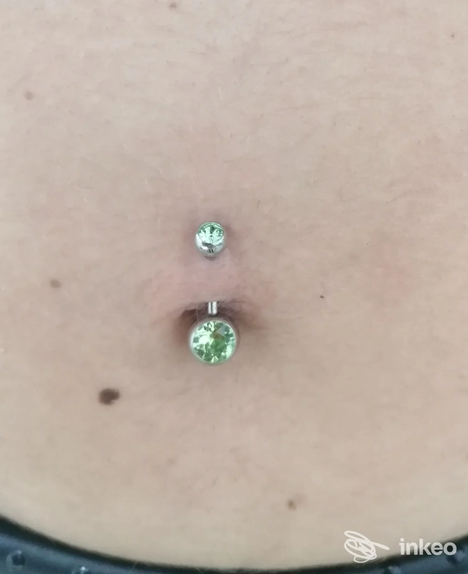 Primo piano di un piercing ombelicale con gioiello a due sfere e cristalli verdi, foto fornita da Crazy di Sabrina Graglia a Cigliano.
