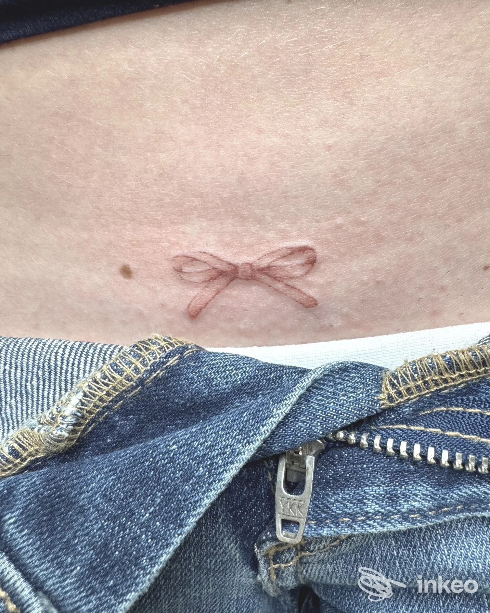 Primo piano di un piccolo tatuaggio a forma di fiocco sul basso ventre, fotografia inviata dallo studio Blue Tony Toy di Firenze.