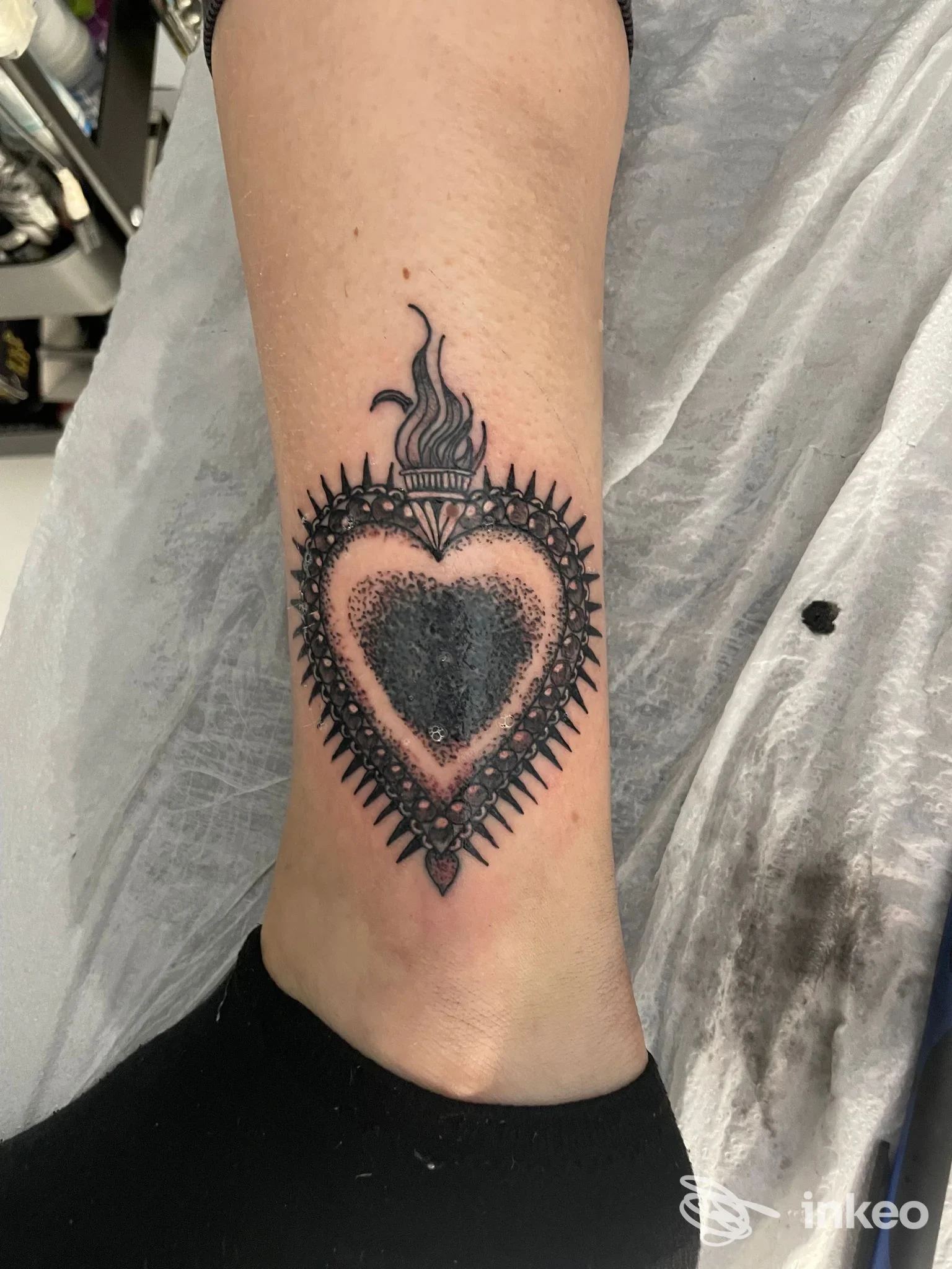 Tatuaggio nero a forma di cuore ornamentale sulla caviglia, immagine fornita da _n1kmark_TattooStudio a Calangianus.