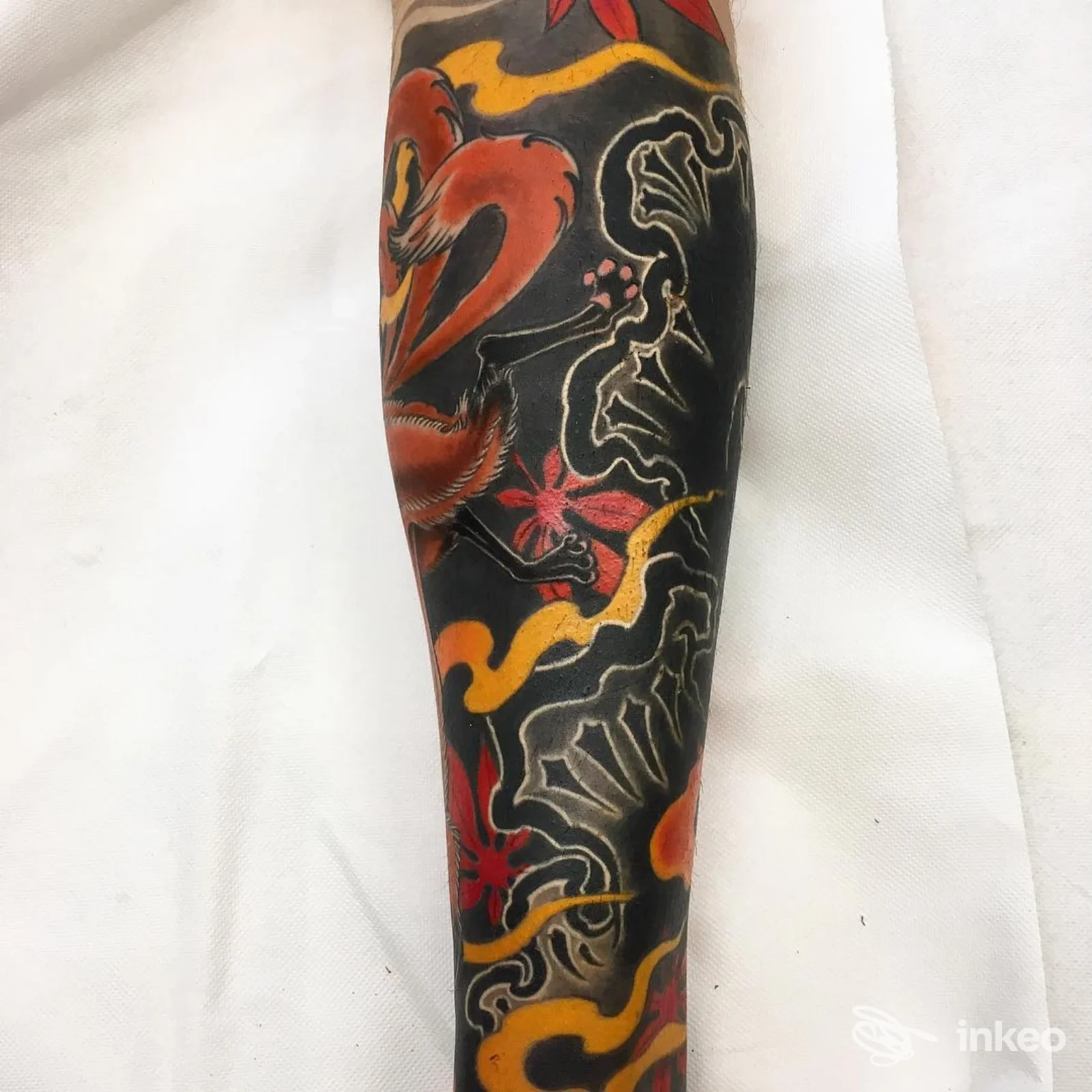 Tatuaggio su avambraccio con ampie aree scure e motivi rossi e gialli, Dr. Frankestein Tattoo, Scandicci.