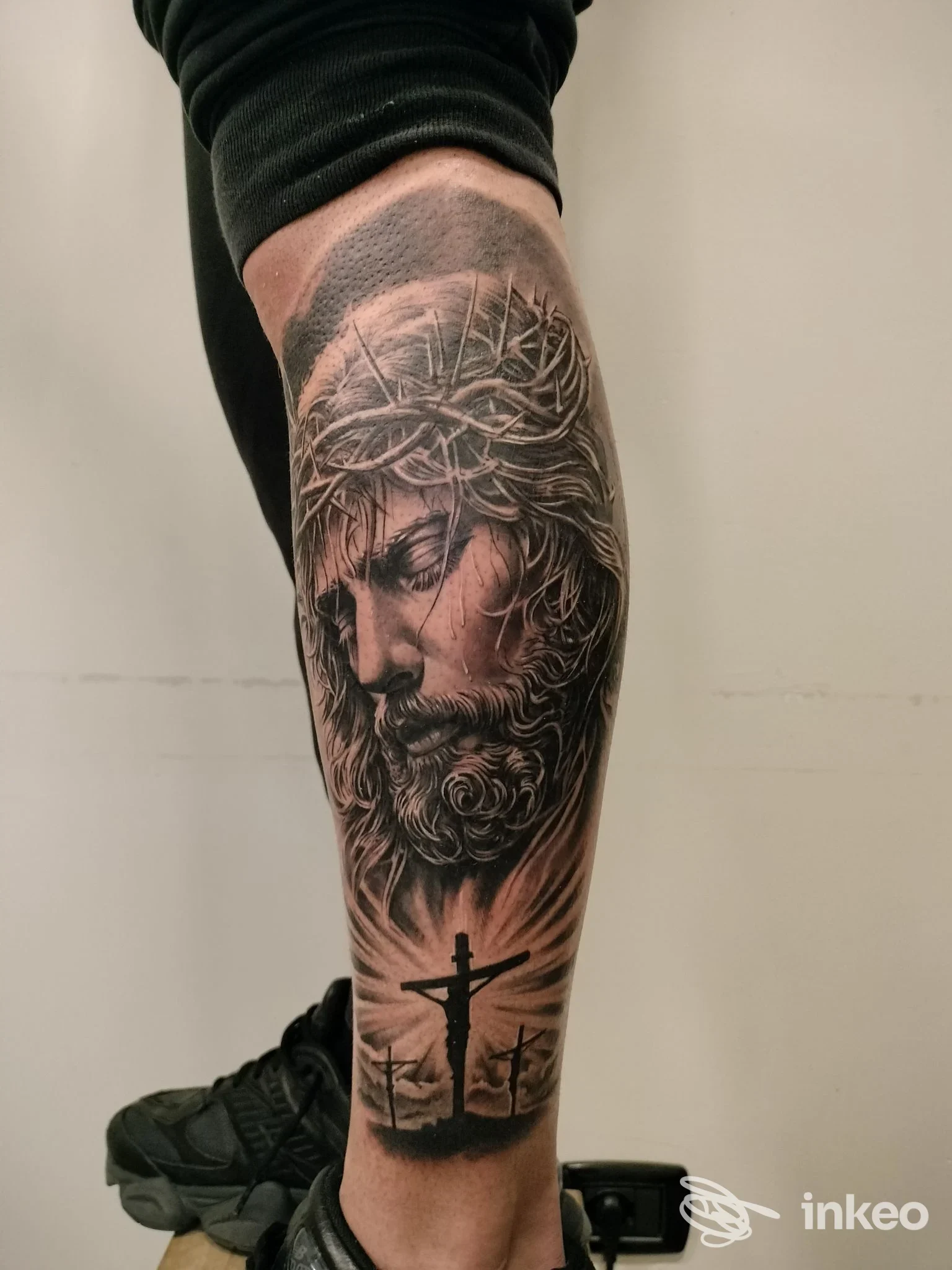 Tatuaggio realistico in bianco e nero sul polpaccio raffigurante il volto di Cristo e la Crocifissione — Andromac'Art Tattoo-Piercing, Agrigento.
