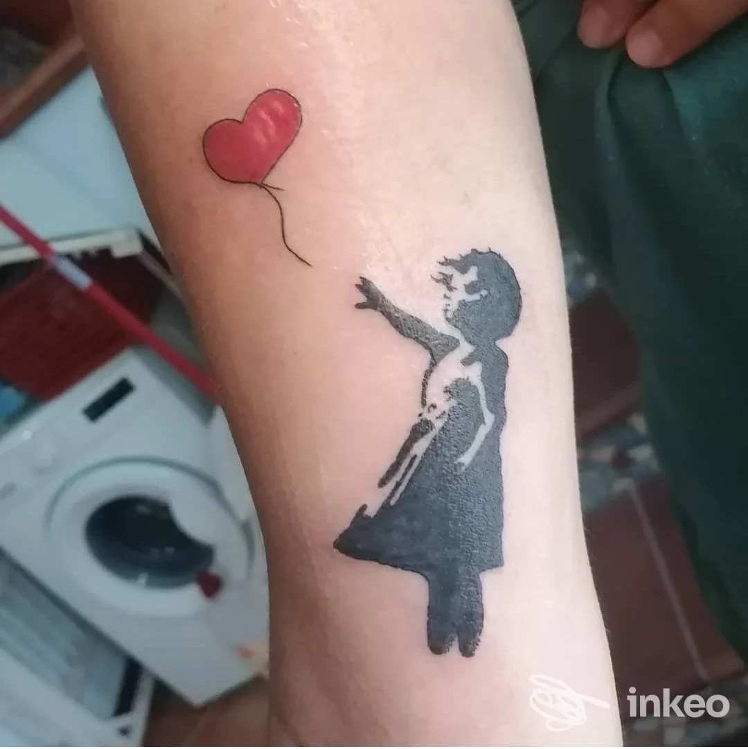 Primo piano di un tatuaggio sull'avambraccio raffigurante una bambina nera che lascia un palloncino a cuore rosso, lavoro realizzato da Ale Ink a Trappeto.