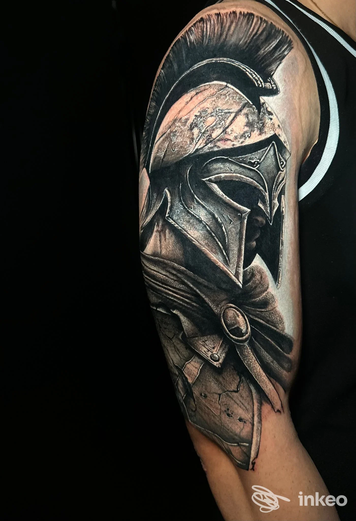 Dettagliato tatuaggio realistico di un elmo spartano sulla parte superiore del braccio, opera presentata da Stylish Tattoo Catania Ink, Catania.