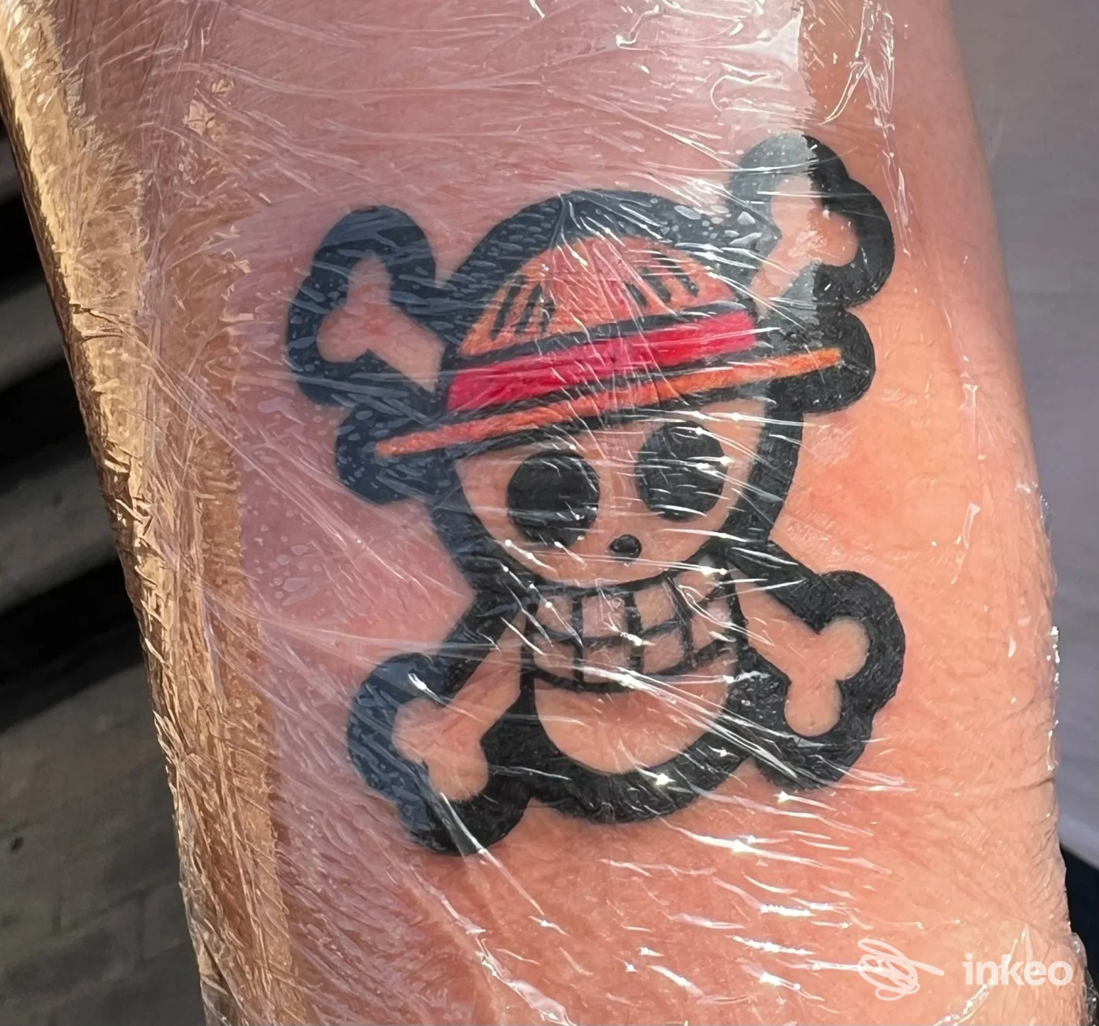 Tatuaggio cartoon di un teschio con ossa incrociate e cappello avvolto nella pellicola sull'avambraccio. Stylish Tattoo Catania Ink, Catania.
