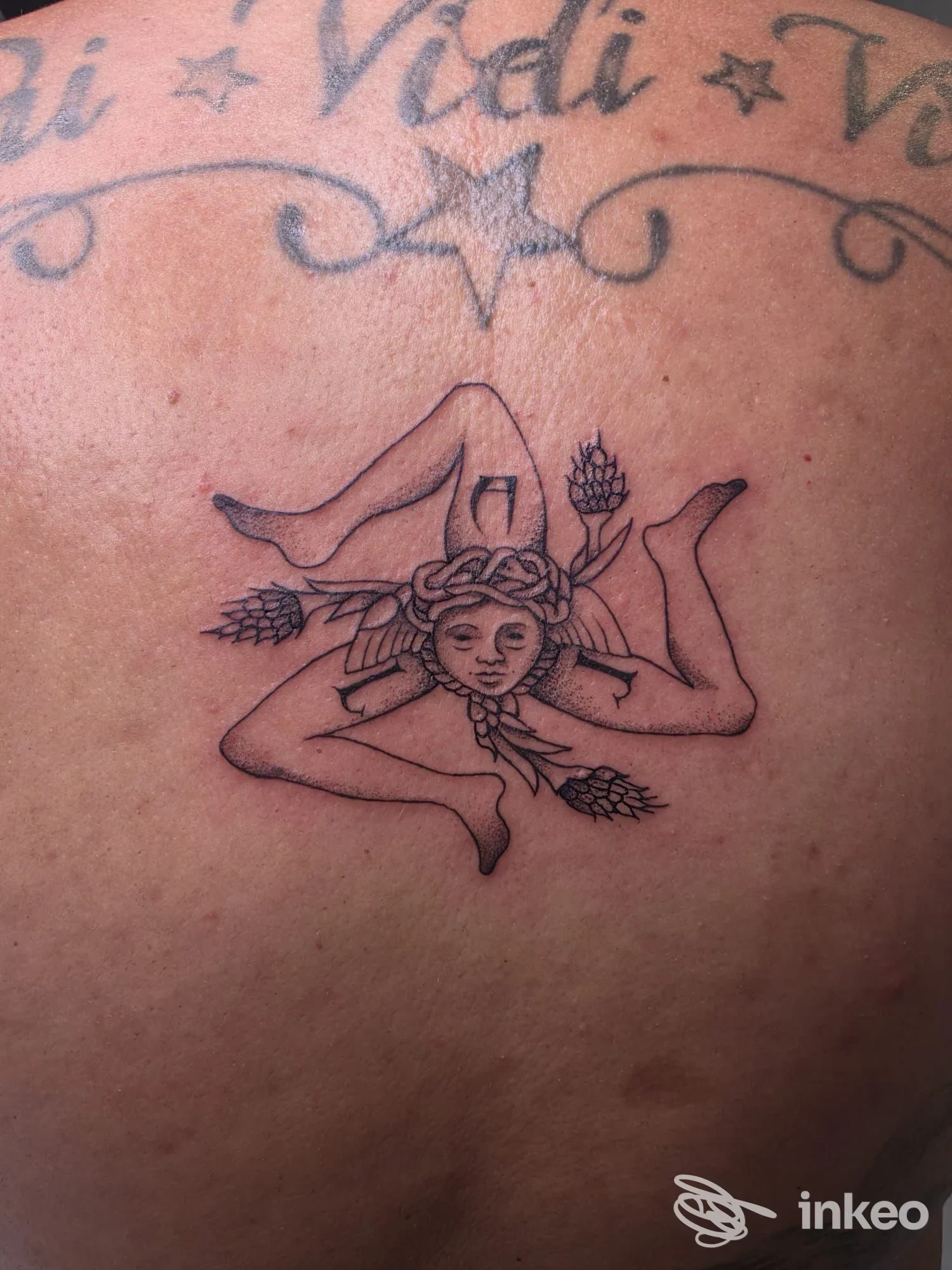 Tatuaggio sul dorso con figura centrale a testa stilizzata e tre gambe, realizzato da Beauty and the beast tattoo studio a Priolo Gargallo.