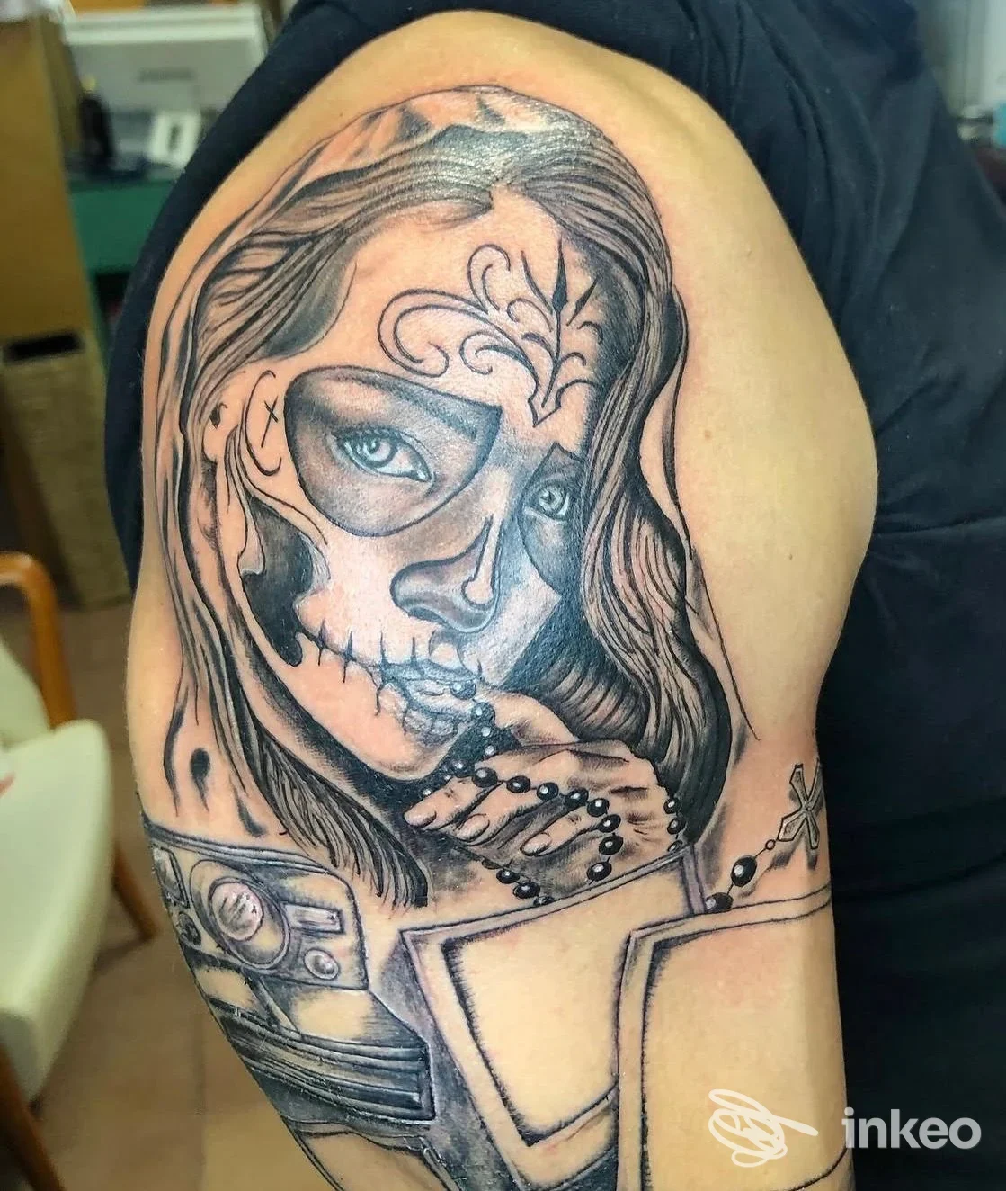 Tatuaggio in bianco e nero su braccio/ spalla raffigurante un volto femminile con maschera scheletrica, Ink & Chic Firenze, Firenze.