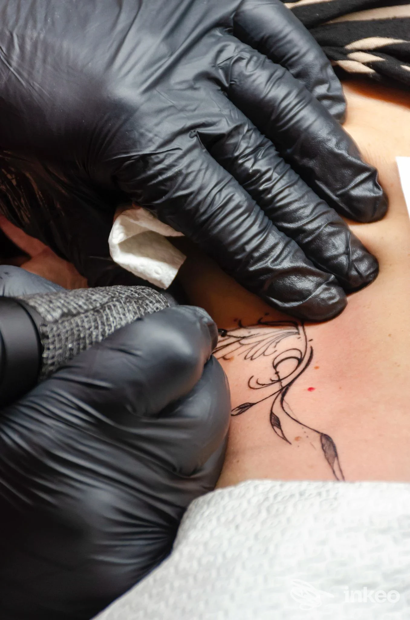 Operatore con guanti neri esegue un tatuaggio ornamentale vicino alla clavicola, foto fornite da Ink & Chic Firenze, Firenze.